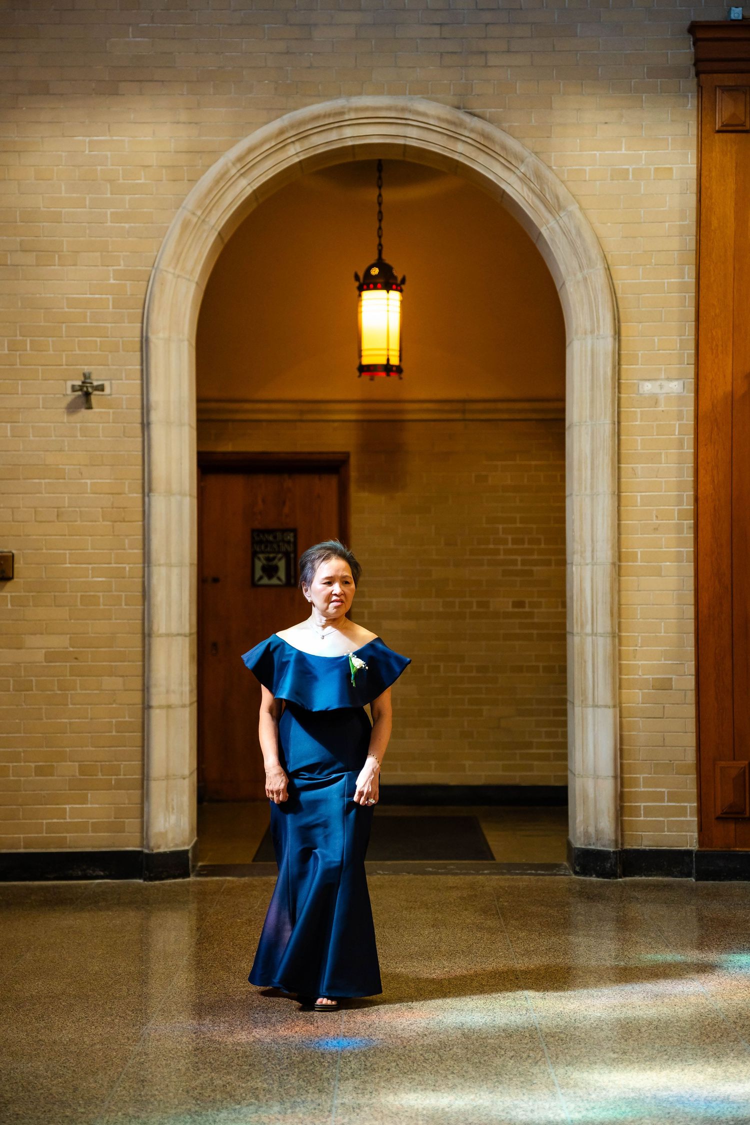Woman in elegant blue off-shoulder mermaid gown standing beneath a stone arch with warm pendant lighting.