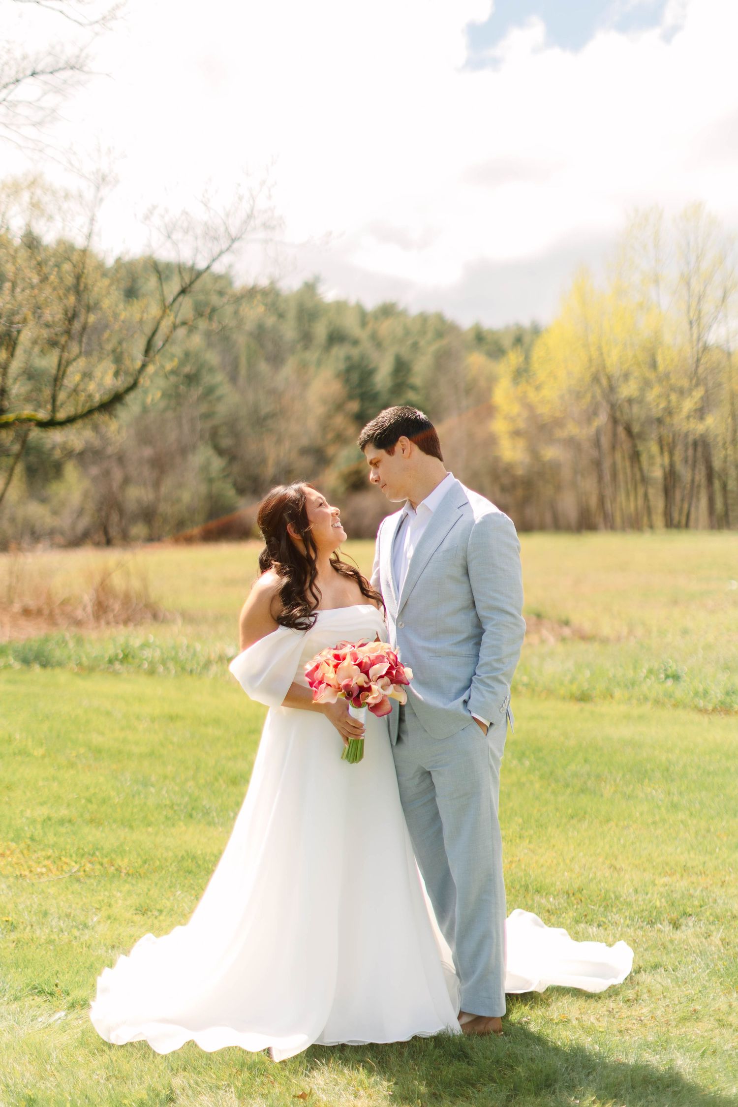Bride and groom share romantic outdoor portrait in green meadow with colorful autumn trees.