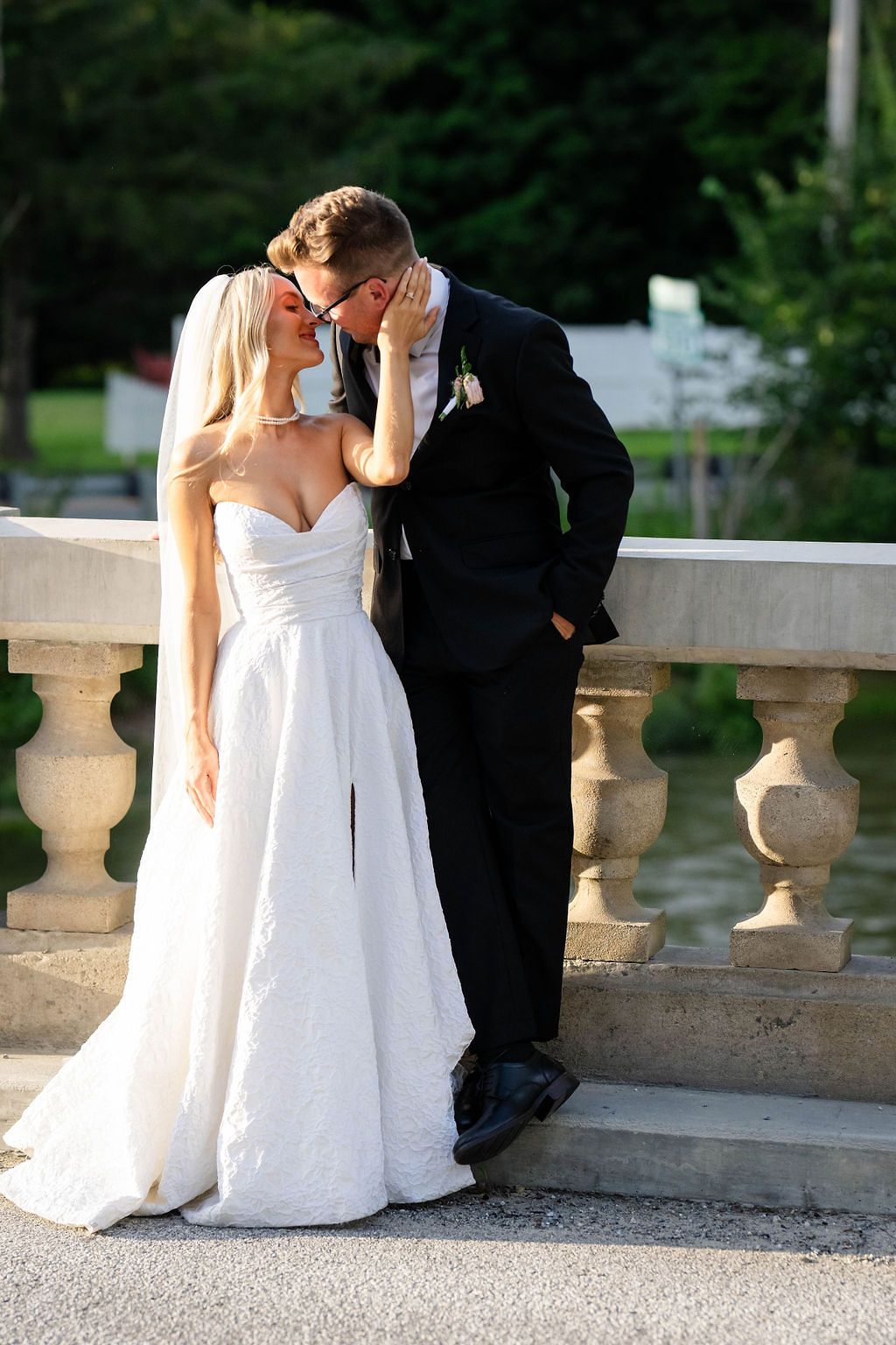 Bride and groom share a romantic kiss on a stone balustrade bridge at golden hour.