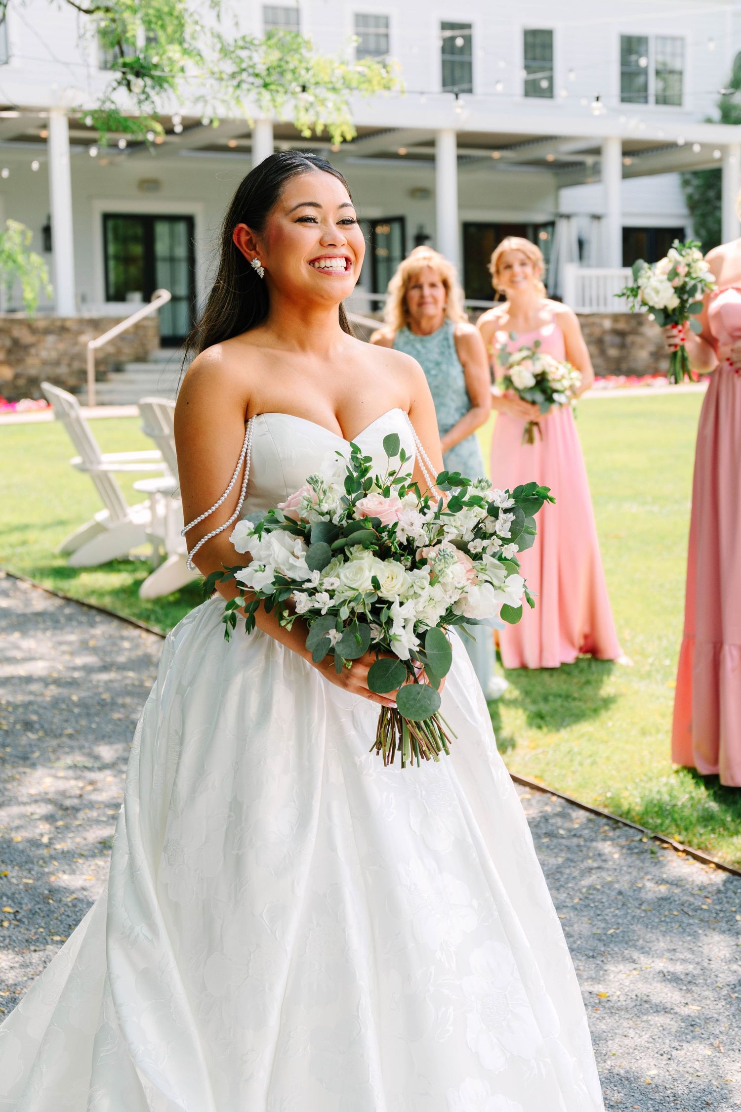 Radiant bride walking down aisle holding white floral bouquet with bridesmaids in pink dresses.