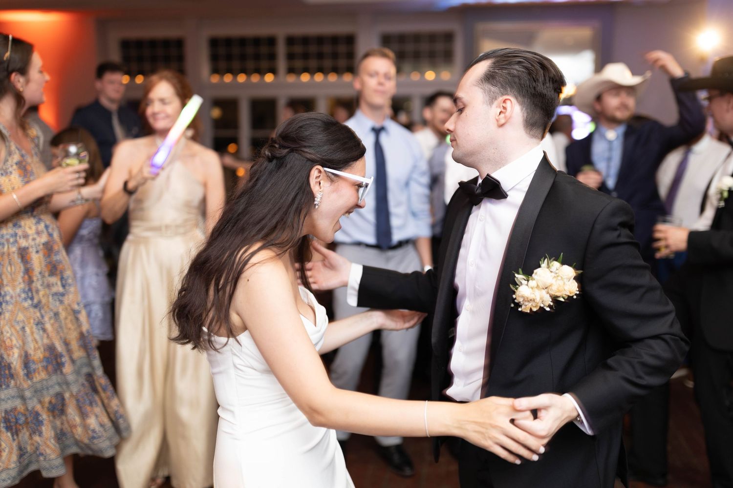 Bride and groom dance joyfully together surrounded by guests at a lively wedding reception.
