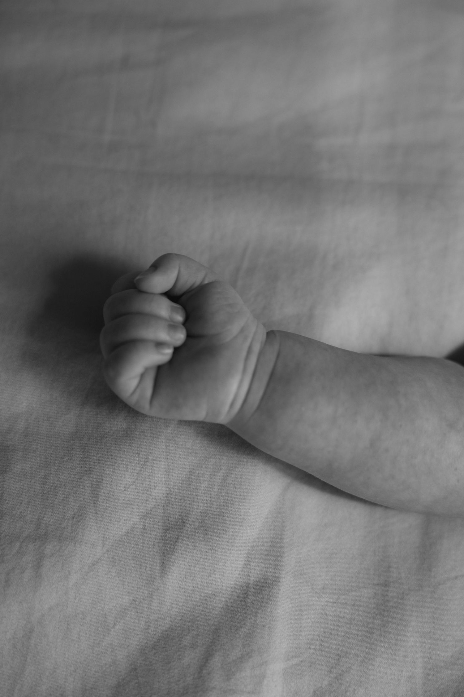 Black and white close-up of a newborn baby's tiny clenched fist resting on soft linen fabric.