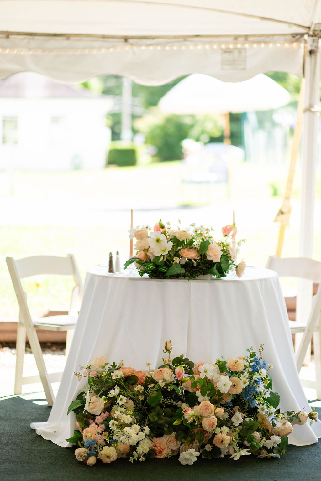 Elegant sweetheart table with white linen and lush pink and blue floral arrangements underneath.