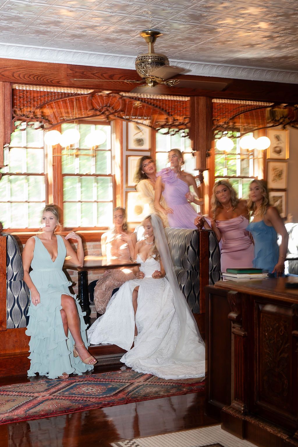 Bride in white gown poses with bridesmaids in colorful dresses inside elegant wood-paneled wedding venue.