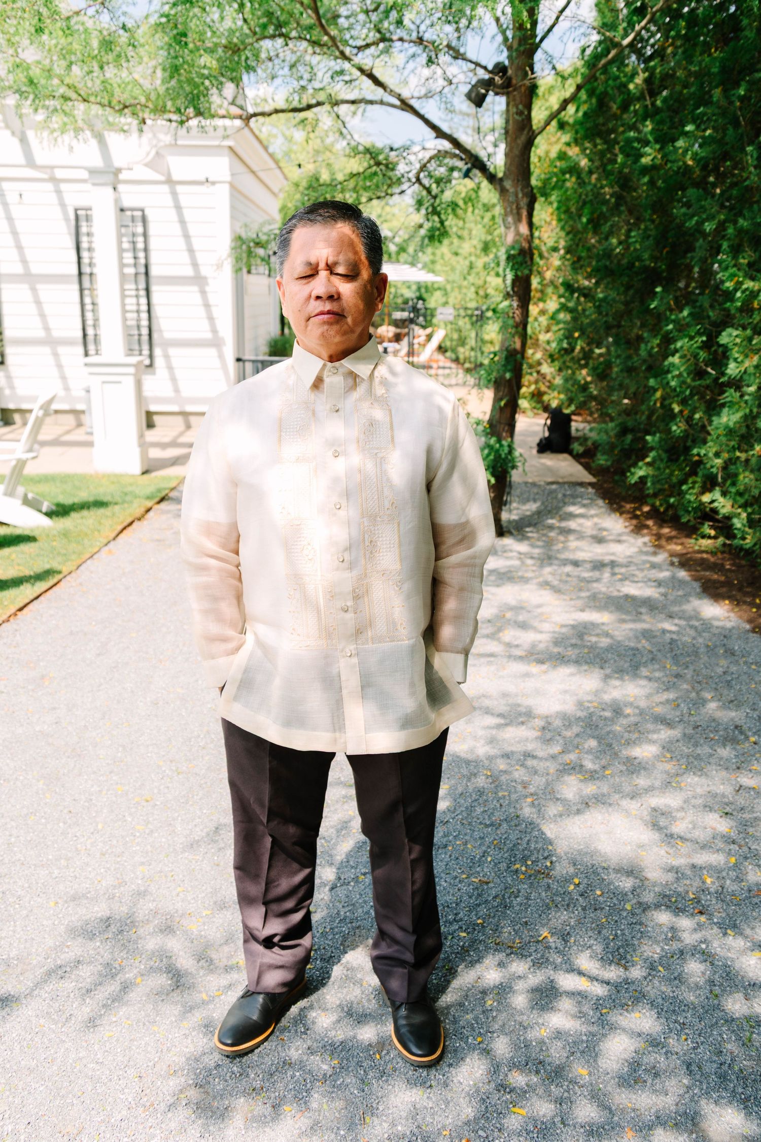 Man wearing traditional Filipino barong tagalog standing on garden pathway at summer wedding.