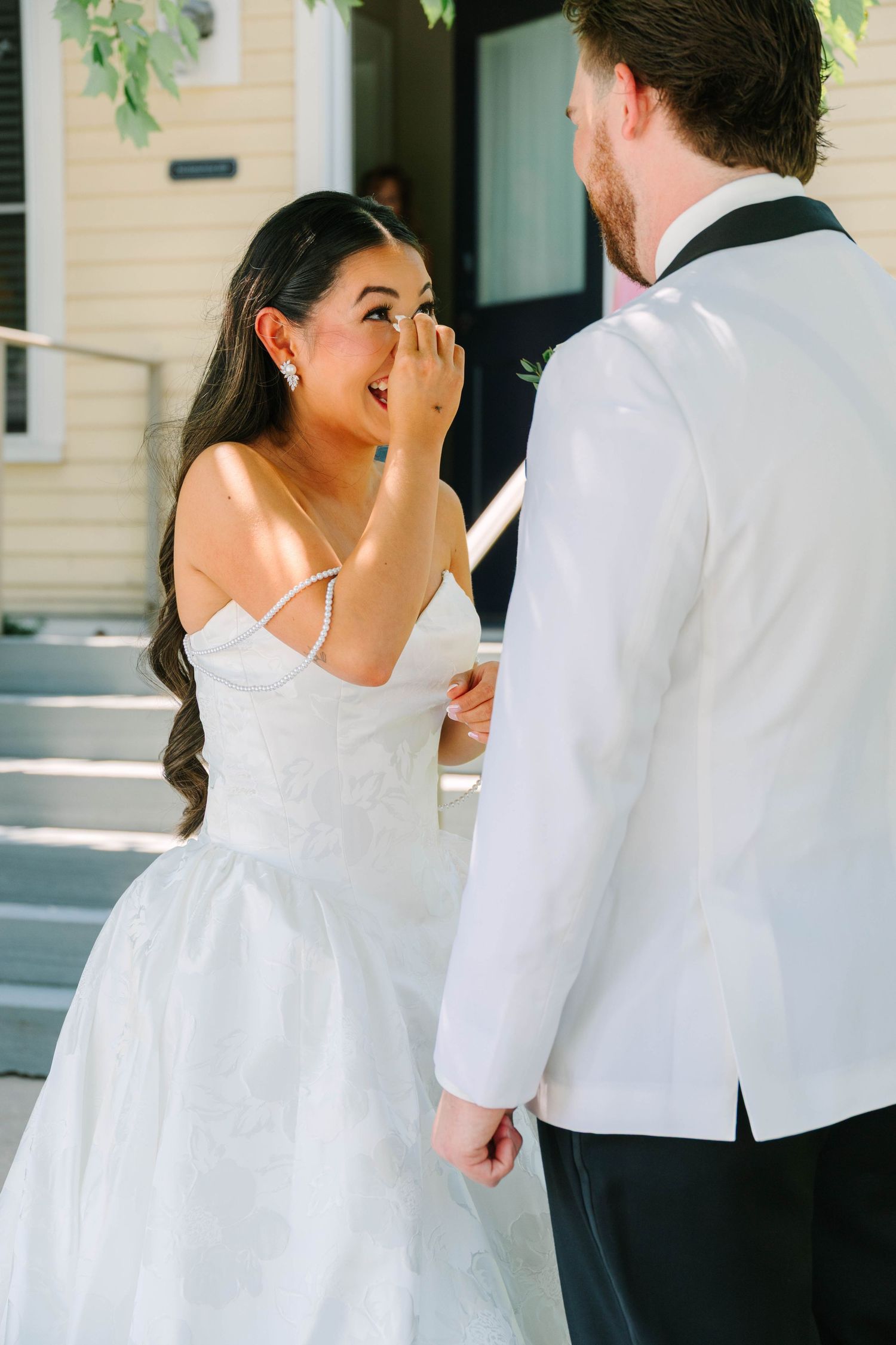 Bride laughing emotionally during first look with groom in white tuxedo jacket on wedding day.