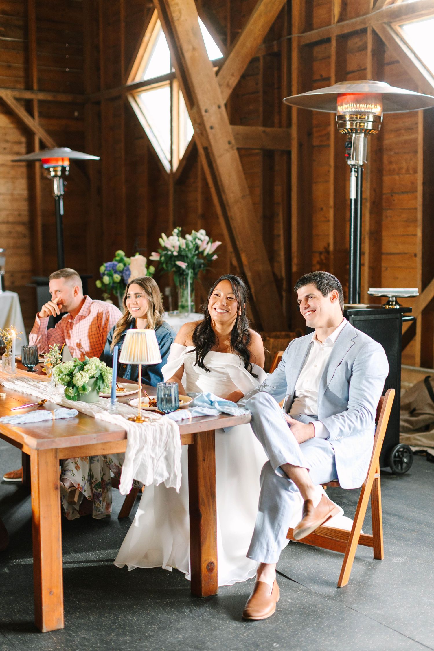 Bride and groom laugh with guests at rustic barn wedding reception with warm wooden interior.