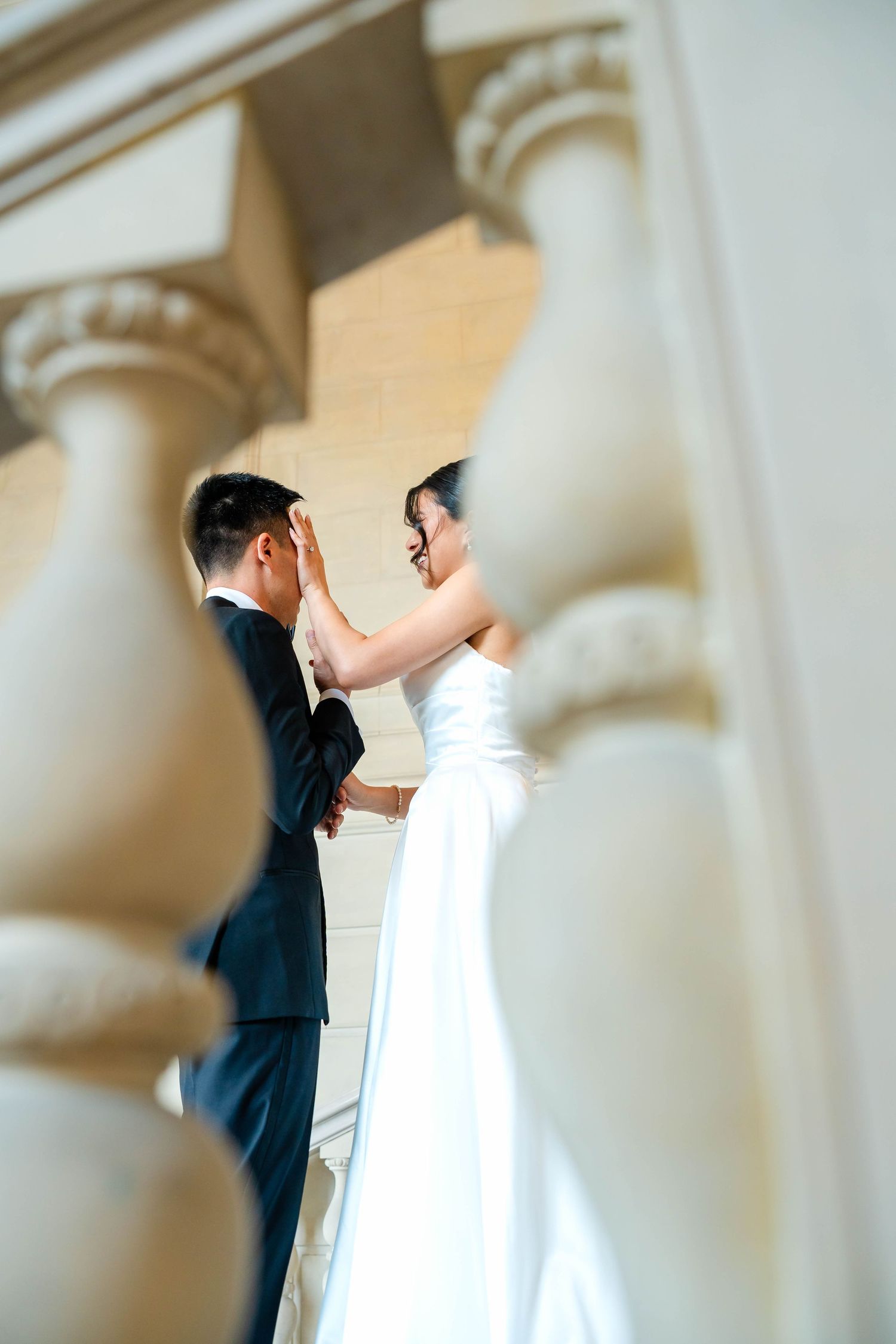 Bride and groom share intimate first look moment between ornate stone columns.