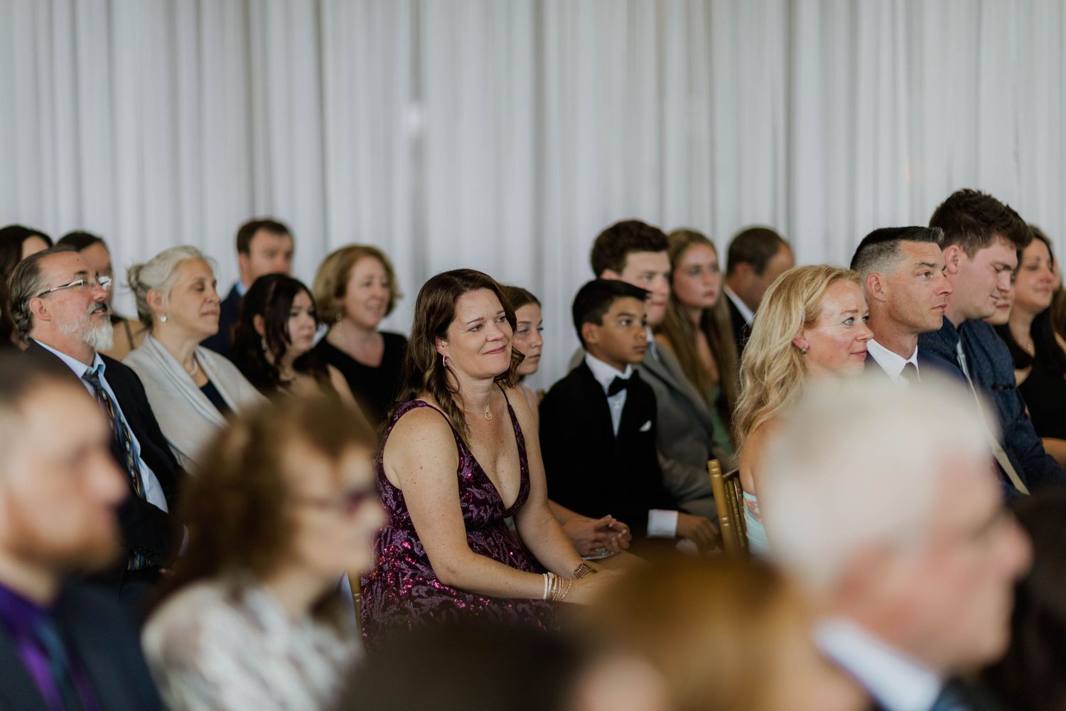 Guests seated at an elegant indoor wedding ceremony, dressed in formal attire, attentively watching the proceedings.