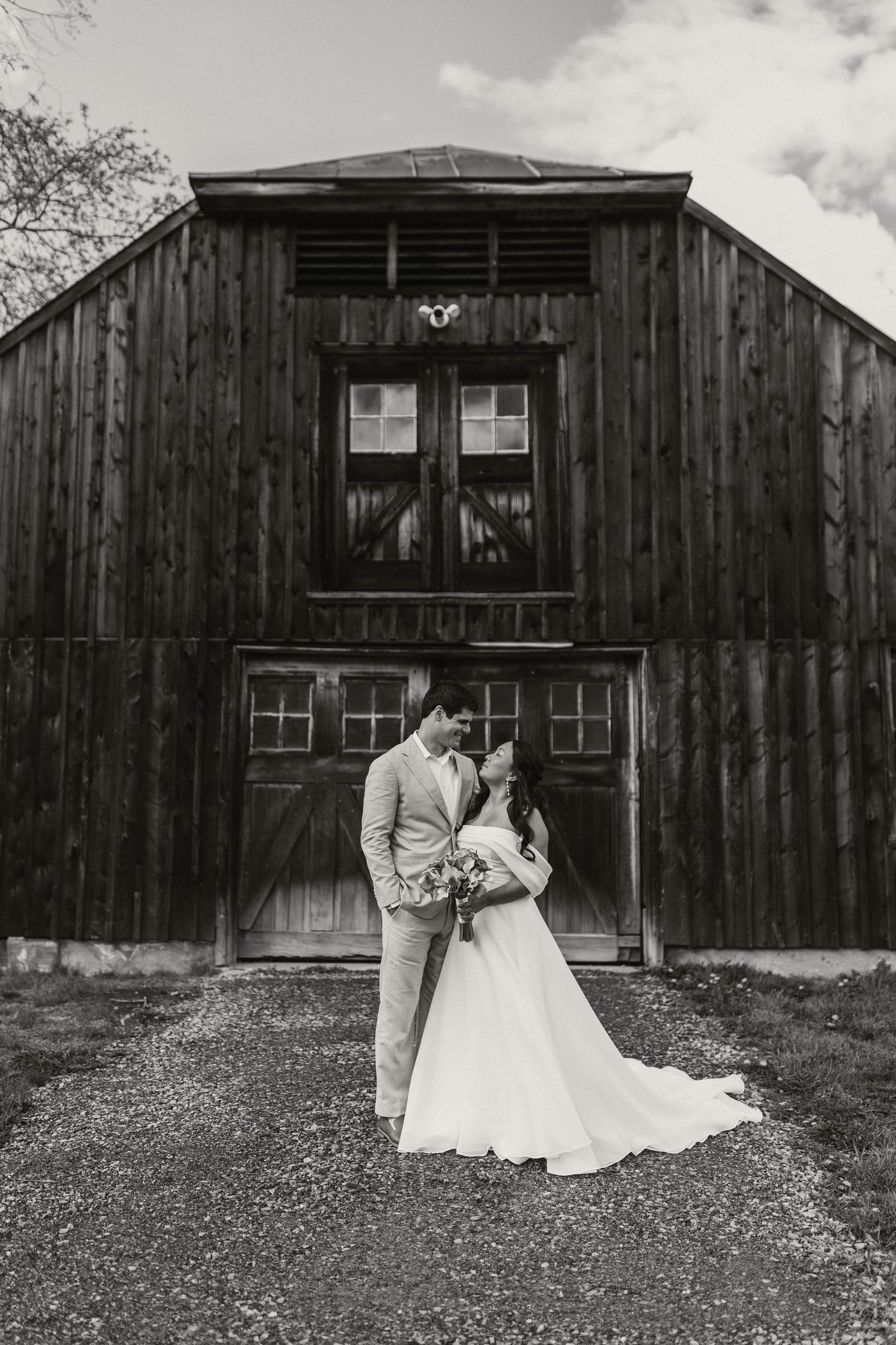 Black and white photo of bride and groom sharing romantic moment in front of rustic barn.