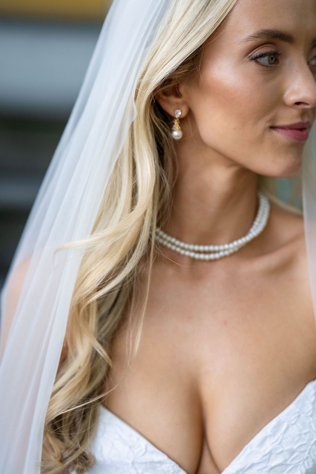 Close-up of blonde bride wearing pearl drop earrings and double-strand pearl necklace with white veil.