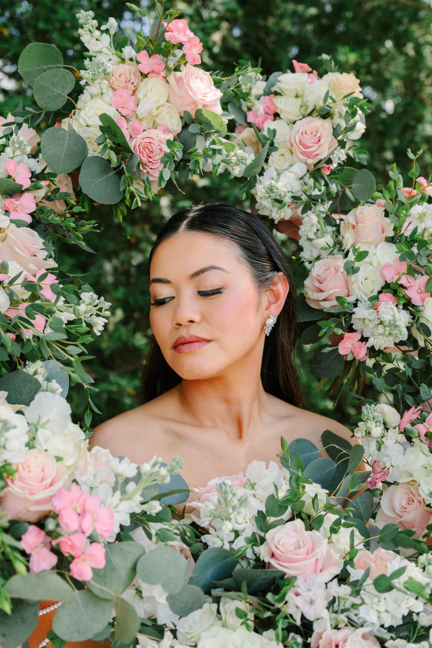 Beautiful bride with closed eyes framed by lush pink roses and white floral wedding bouquets.