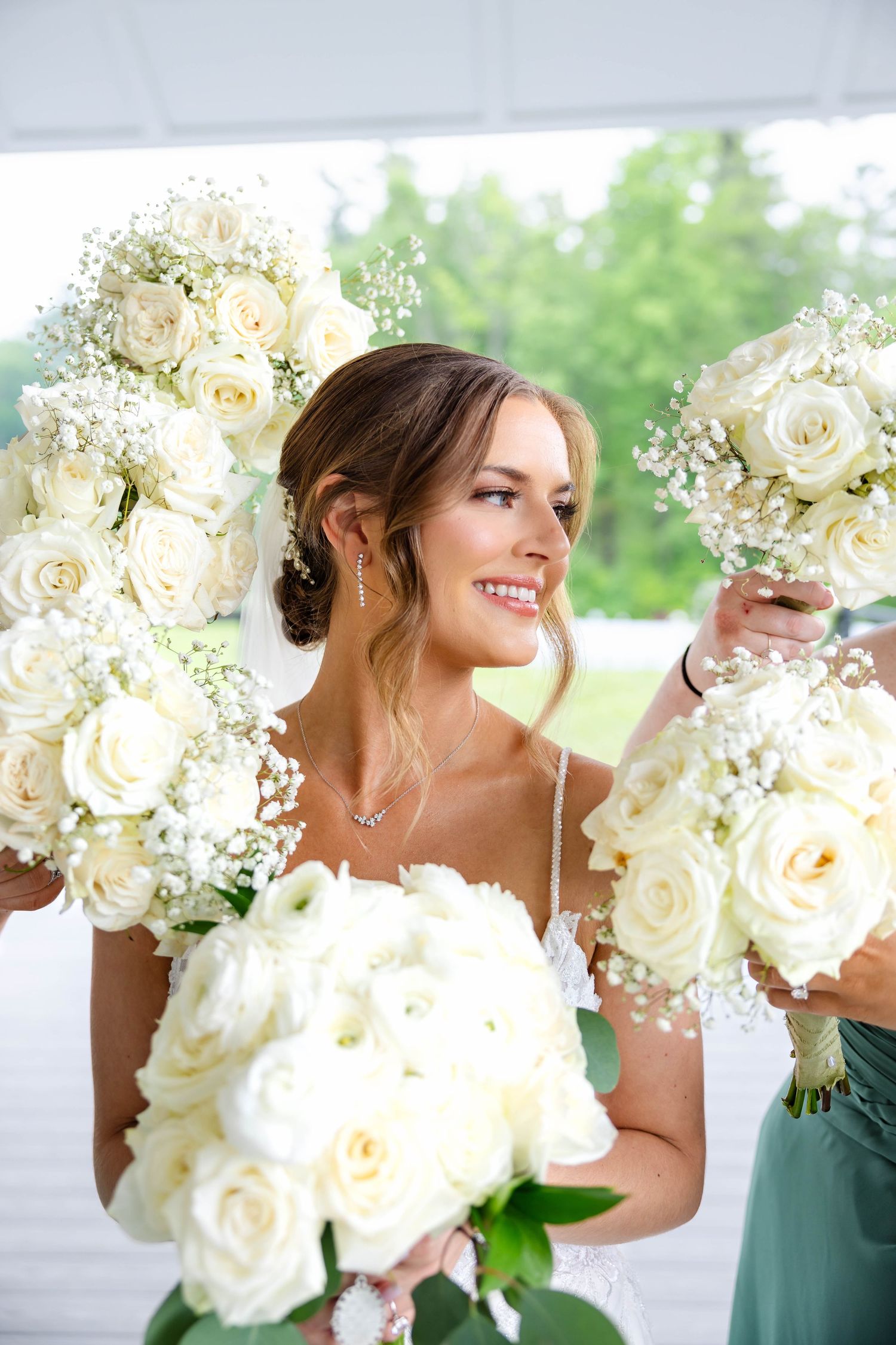 Beautiful bride surrounded by white rose and baby's breath bouquets smiling on wedding day.