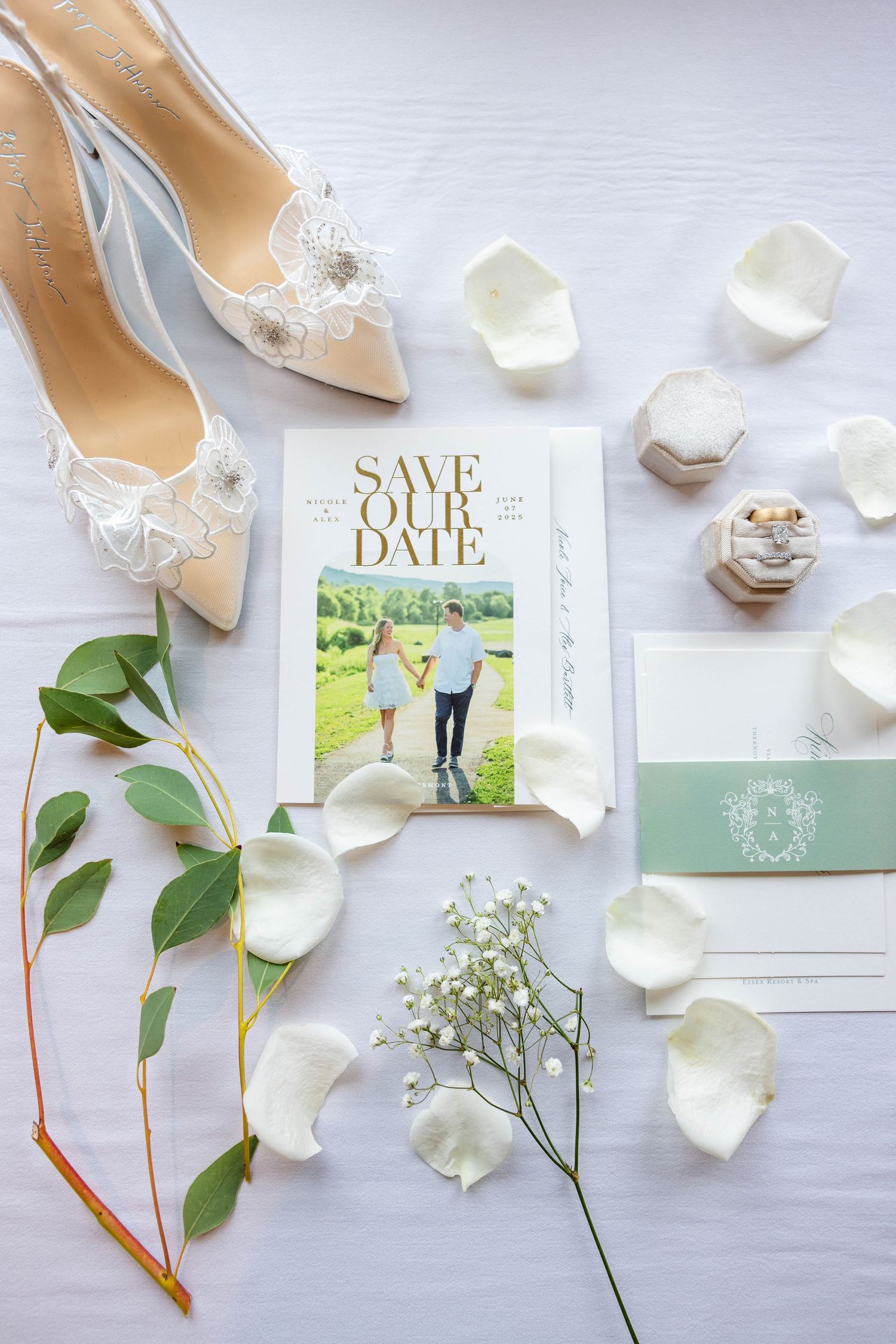 Elegant wedding flat lay with lace bridal heels, save the date card, green envelope, rose petals, and diamond rings.