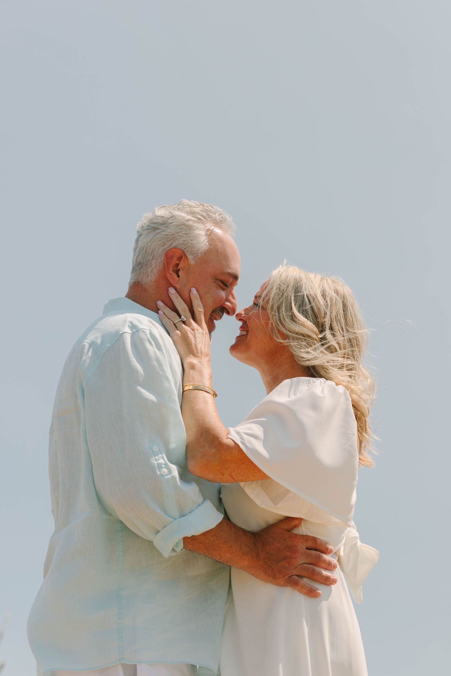 Romantic senior couple embracing and about to kiss outdoors against a clear blue sky.