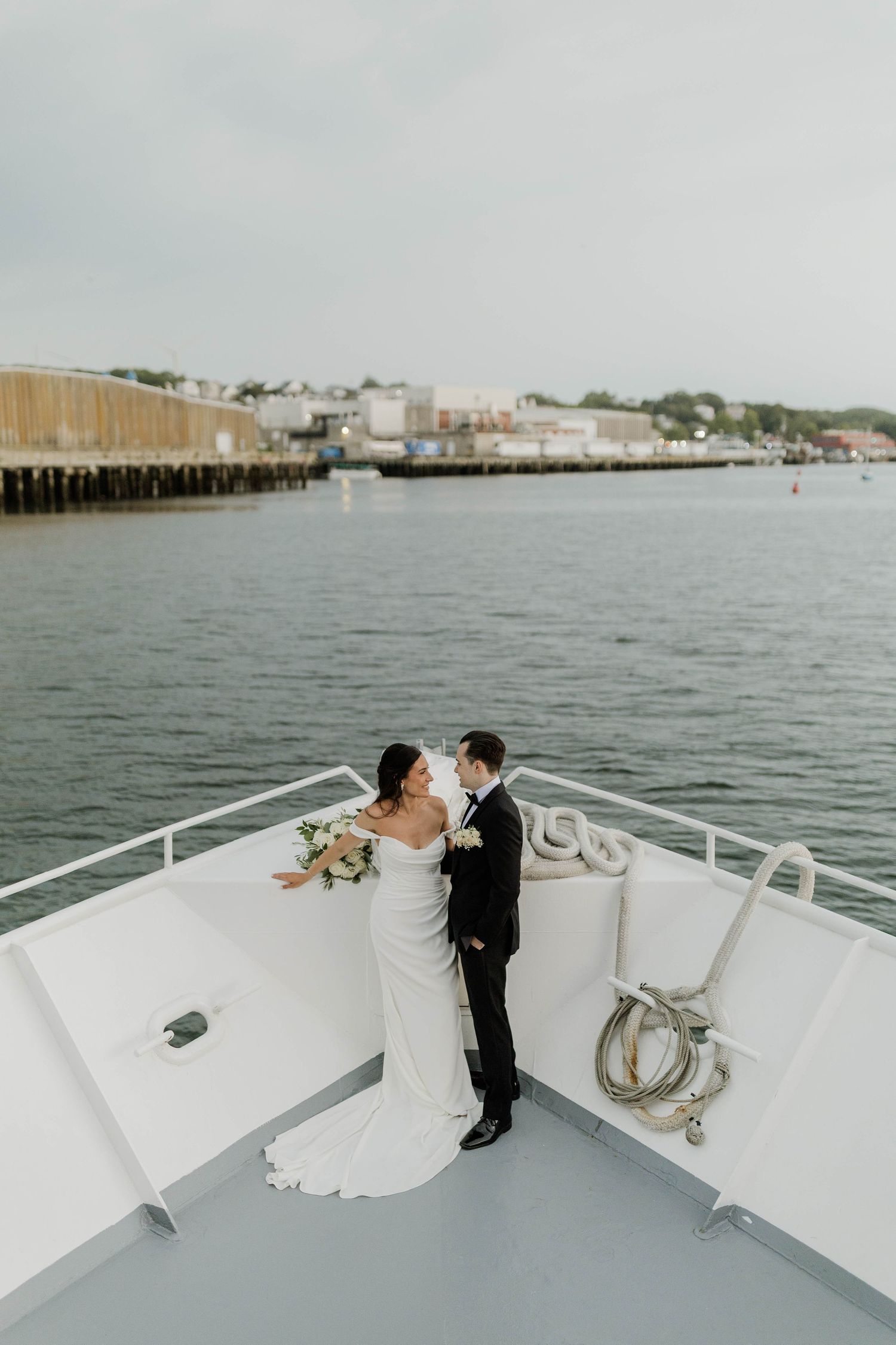Bride and groom sharing a romantic moment on the bow of a yacht with waterfront views.