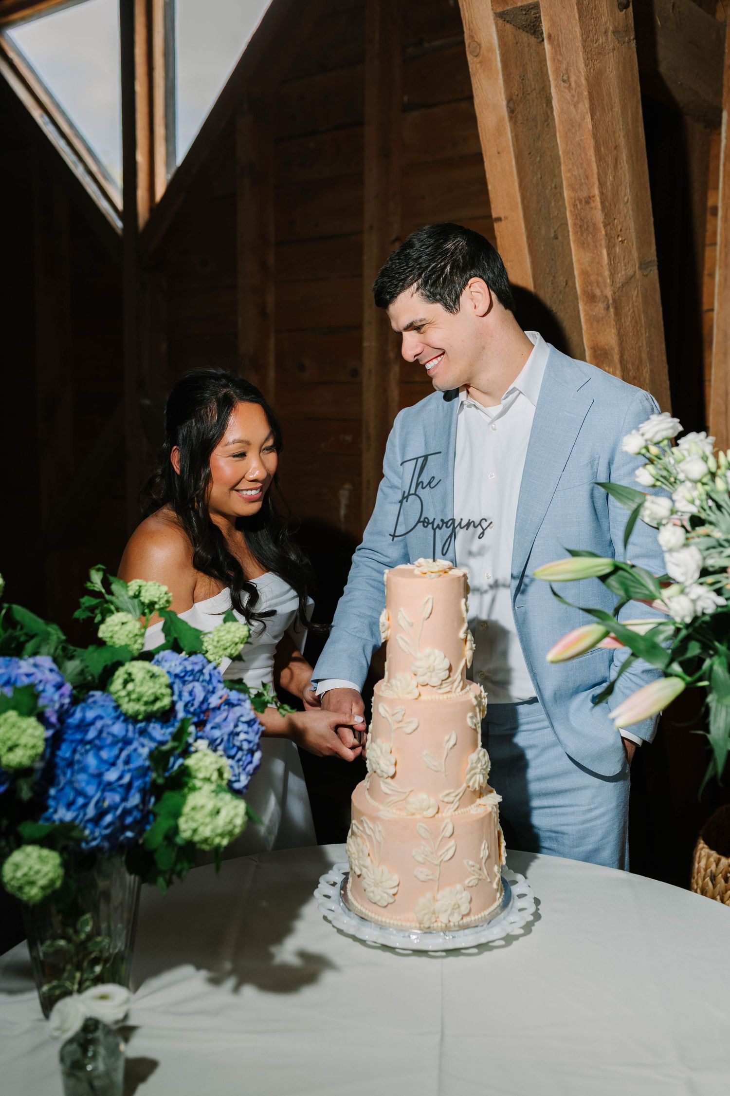 Bride and groom cutting a four-tier peach wedding cake surrounded by blue hydrangeas.