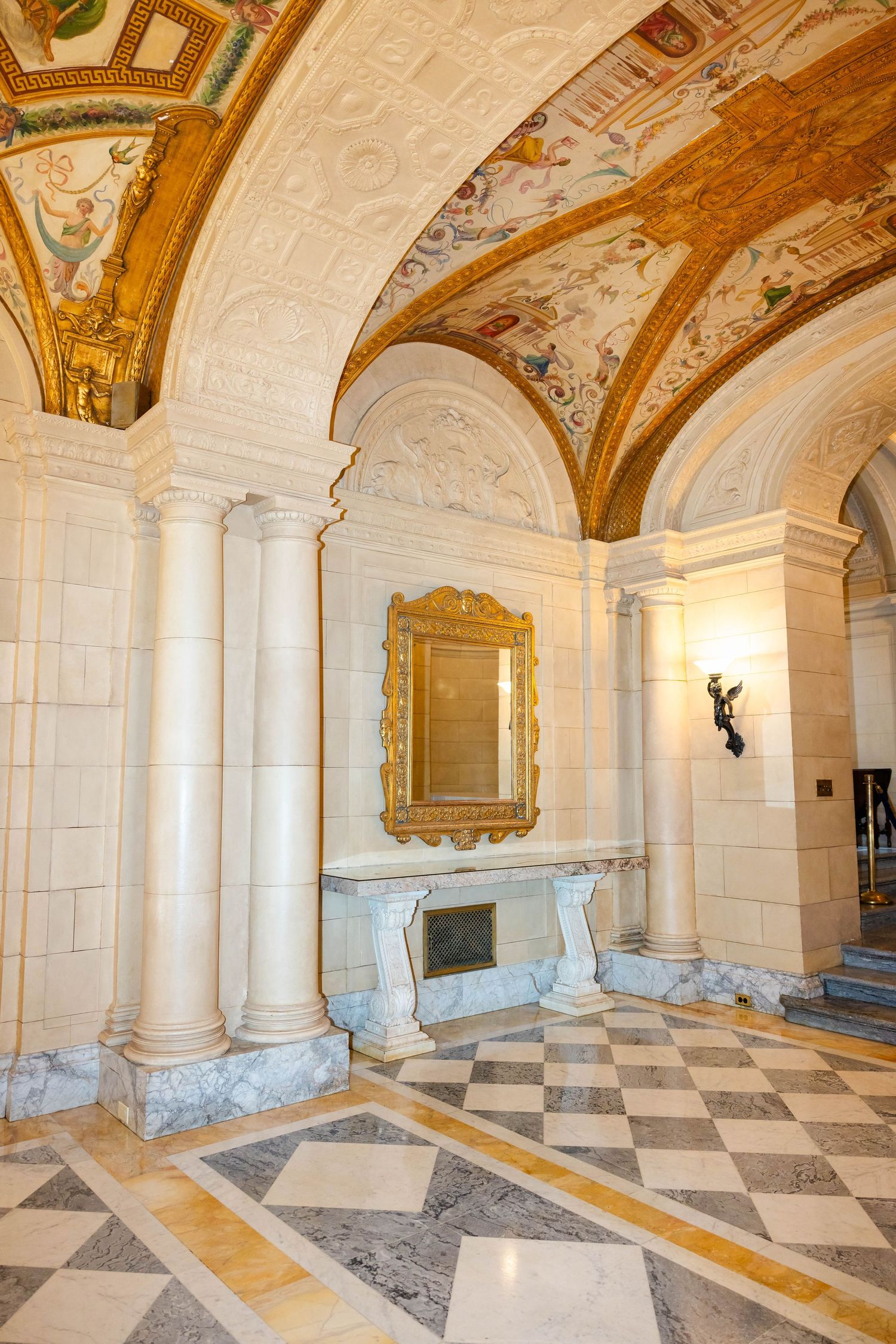 Ornate marble hallway with gilded vaulted ceiling, columns, and decorative gold mirror.