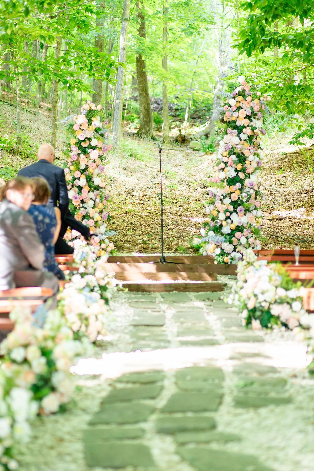 Outdoor wedding ceremony aisle lined with floral arrangements leading to a flower-covered arch.