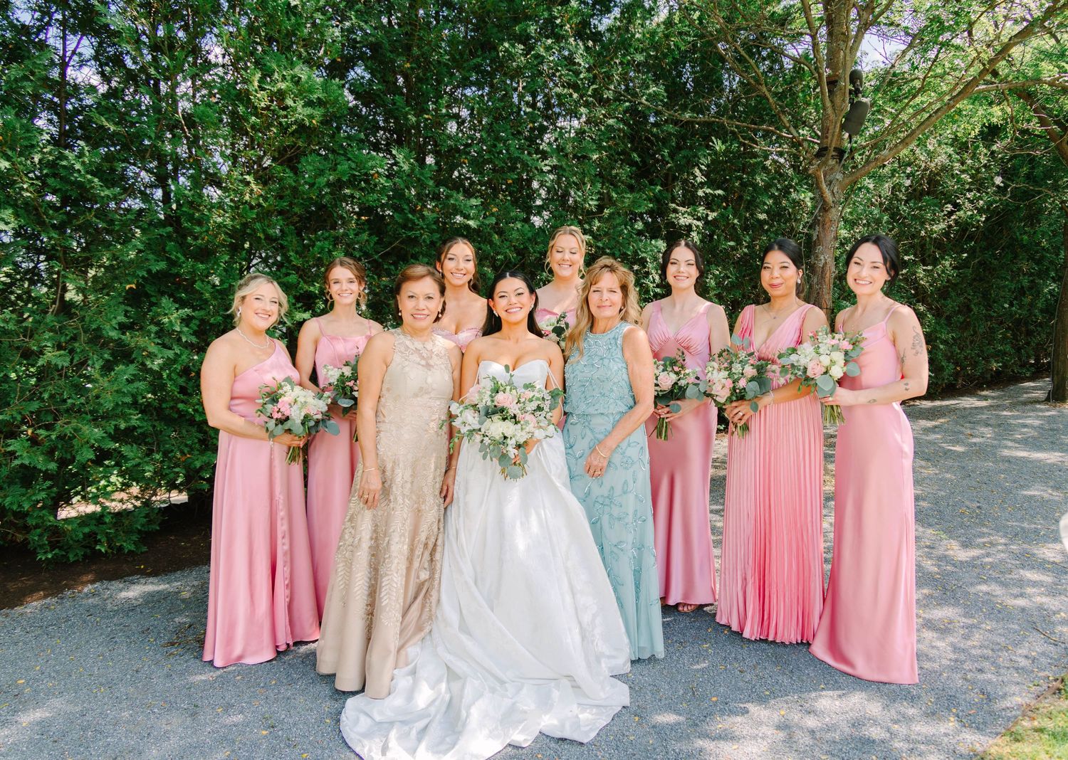 Wedding party group photo with bride, bridesmaids in pink and blue gowns holding floral bouquets.