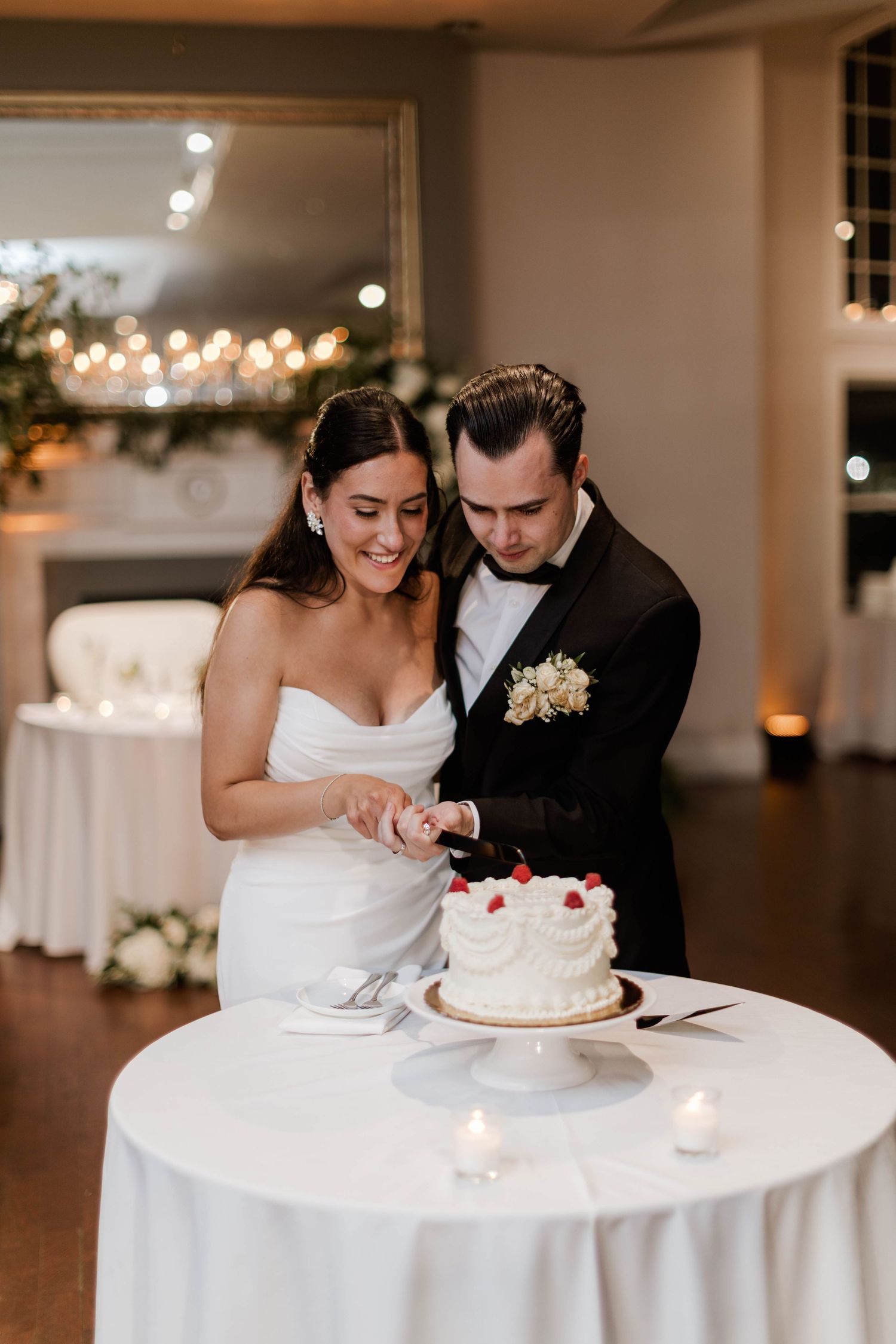 Bride and groom cutting their white wedding cake topped with raspberries at their elegant reception.