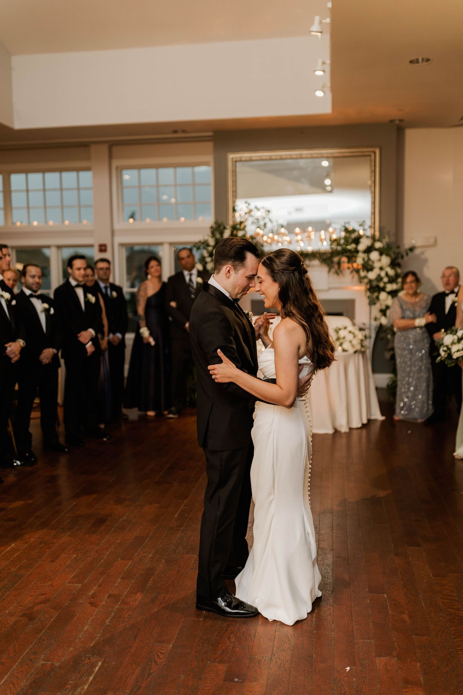 Newlyweds sharing intimate first dance embrace at romantic wedding reception with floral backdrop.