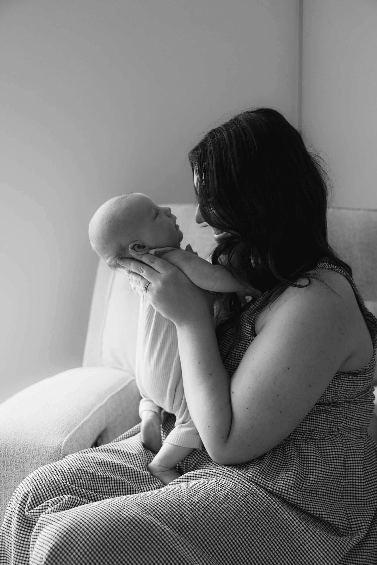Black and white photo of a mother tenderly holding her newborn baby on a chair.