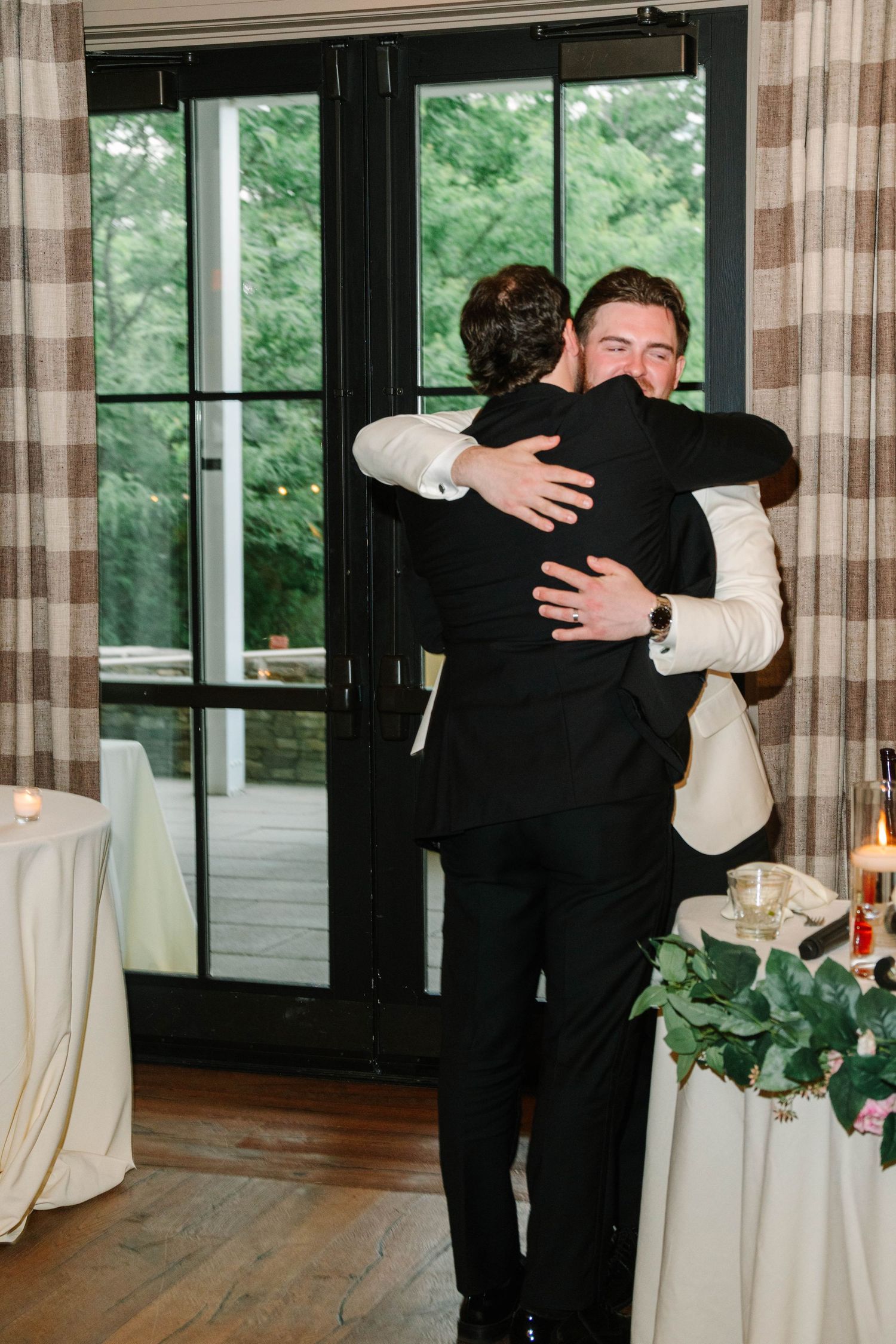 Groom in white jacket embraces best man in emotional hug after heartfelt wedding speech.