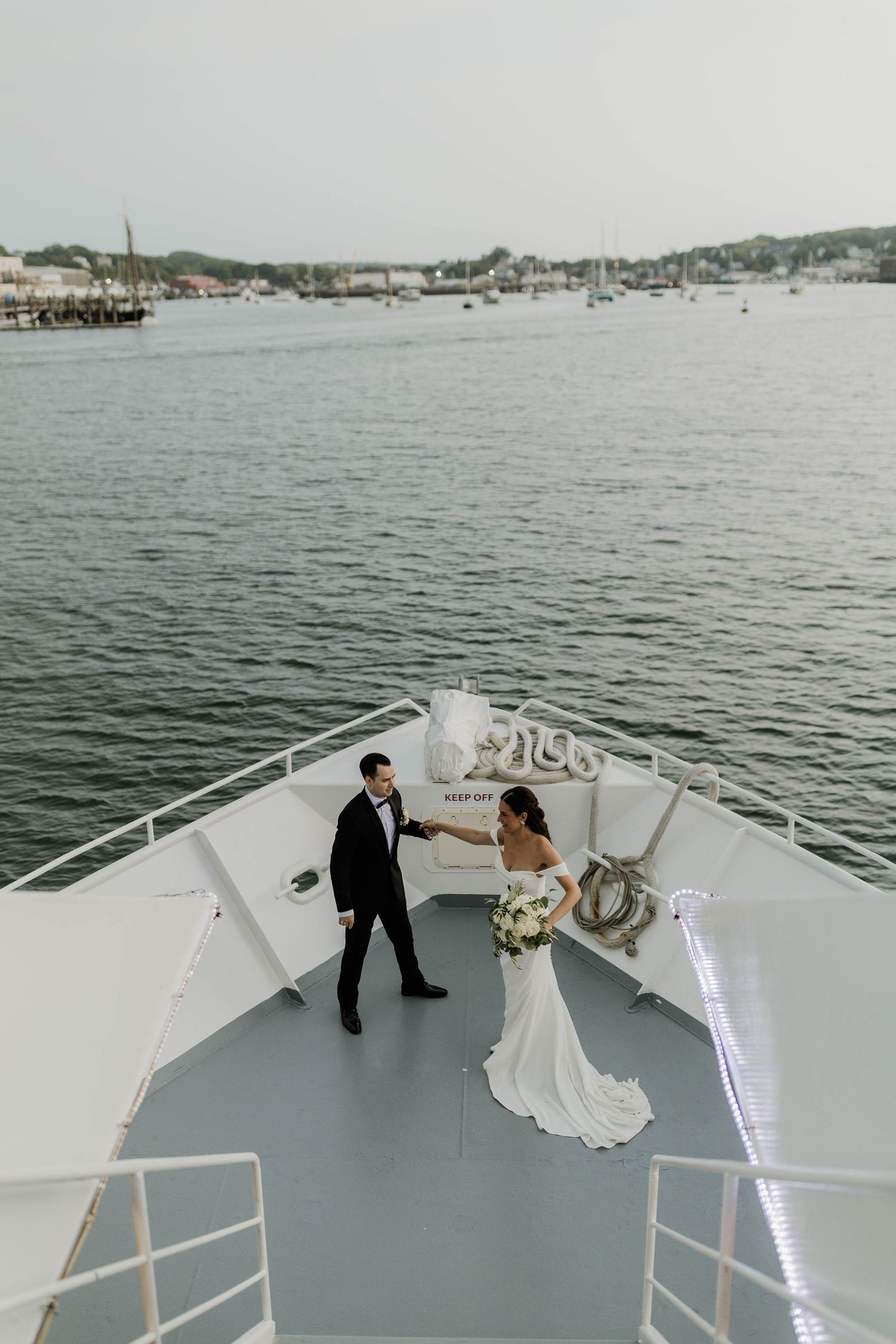 Bride and groom share a romantic moment on the bow of a yacht with harbor views in the background.