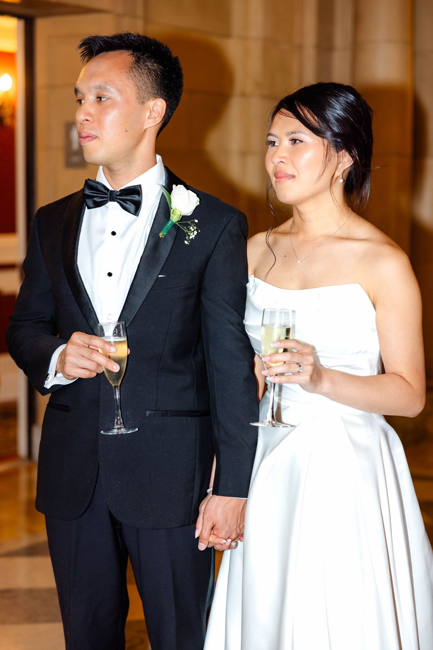 Bride and groom holding champagne glasses and hands during wedding reception toasts in elegant venue.