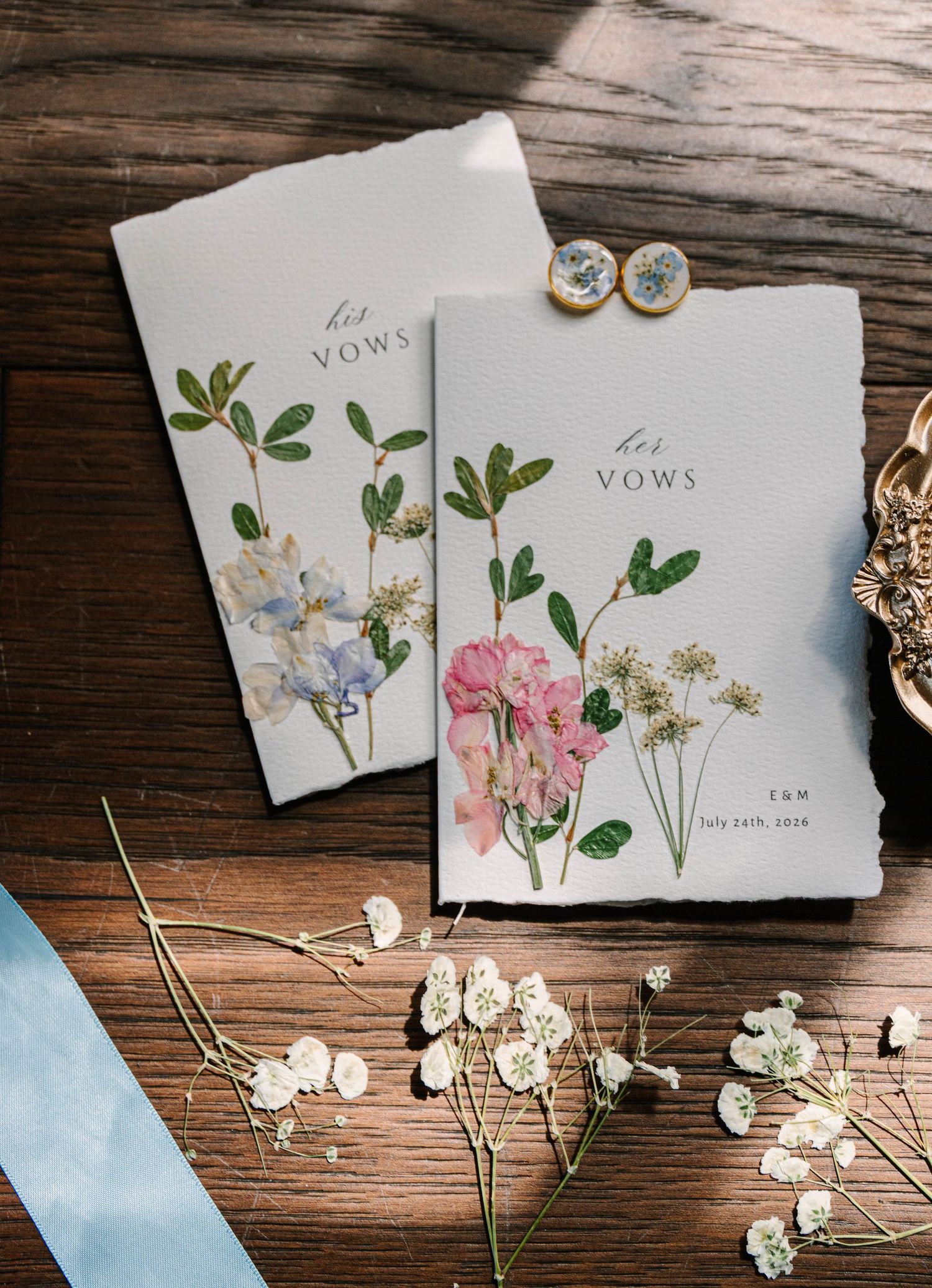 Elegant botanical floral vow booklets with pressed flower designs on rustic wooden table surface.