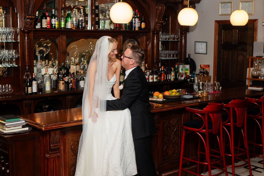 Bride and groom share a romantic embrace at a elegant wooden bar during their wedding reception.