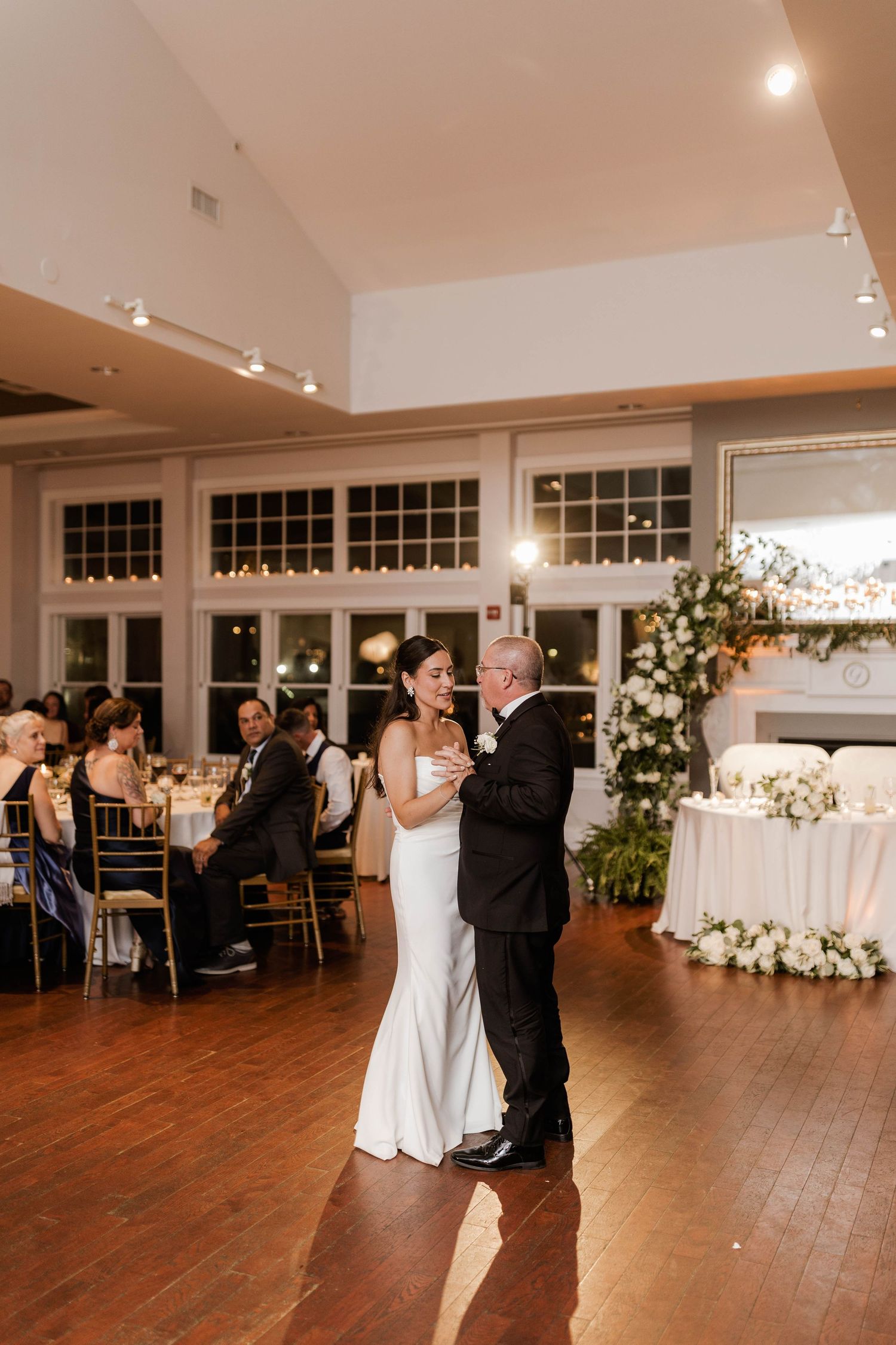 Bride dancing with father on wooden dance floor at elegant wedding reception.