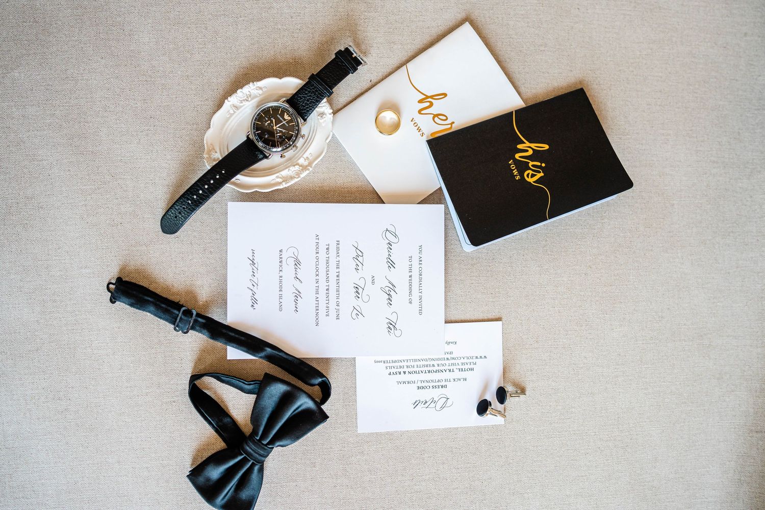 Wedding flat lay featuring black bow tie, watch, invitation suite, and gold jewelry accessories.