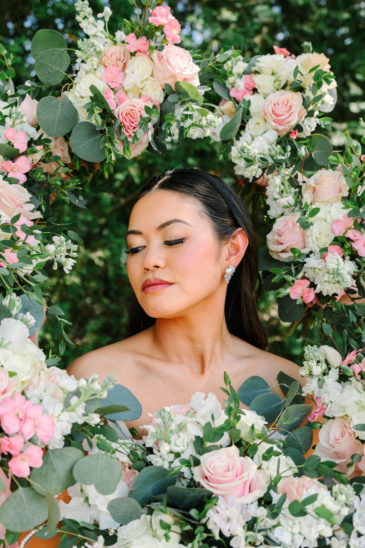 Elegant bride with closed eyes surrounded by a stunning arrangement of pink and white roses.