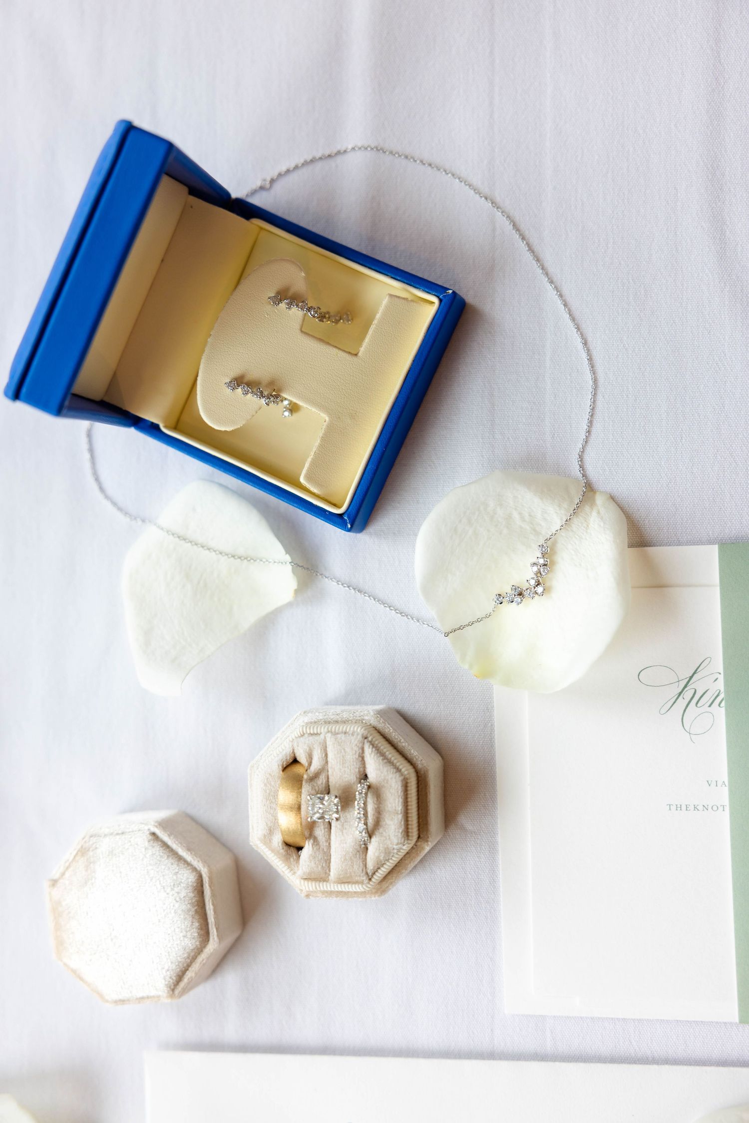 Wedding jewelry flat lay featuring diamond earrings in blue box, necklace, and rings in velvet box.