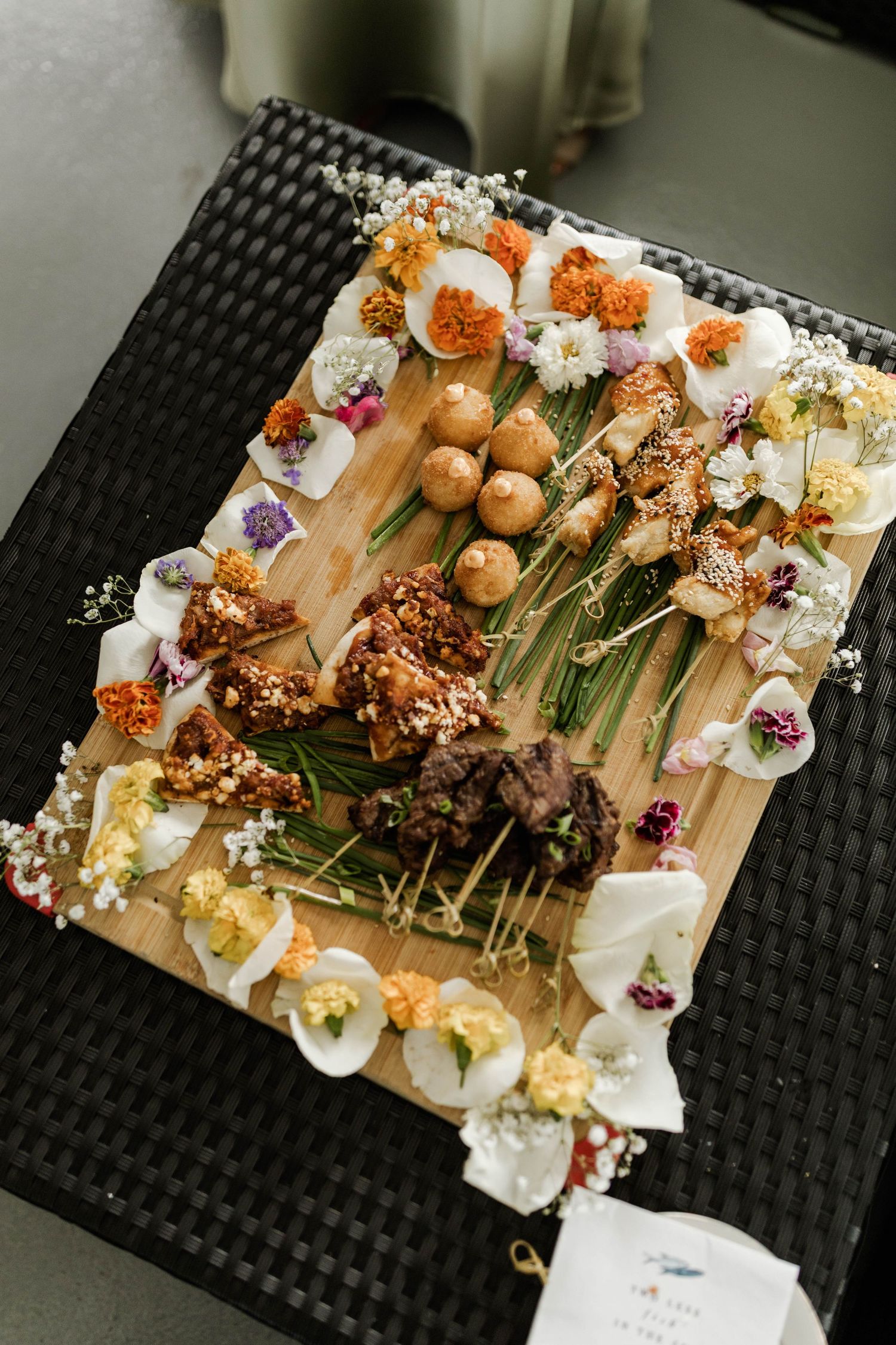 Elegant wedding charcuterie board decorated with colorful edible flowers and skewers.
