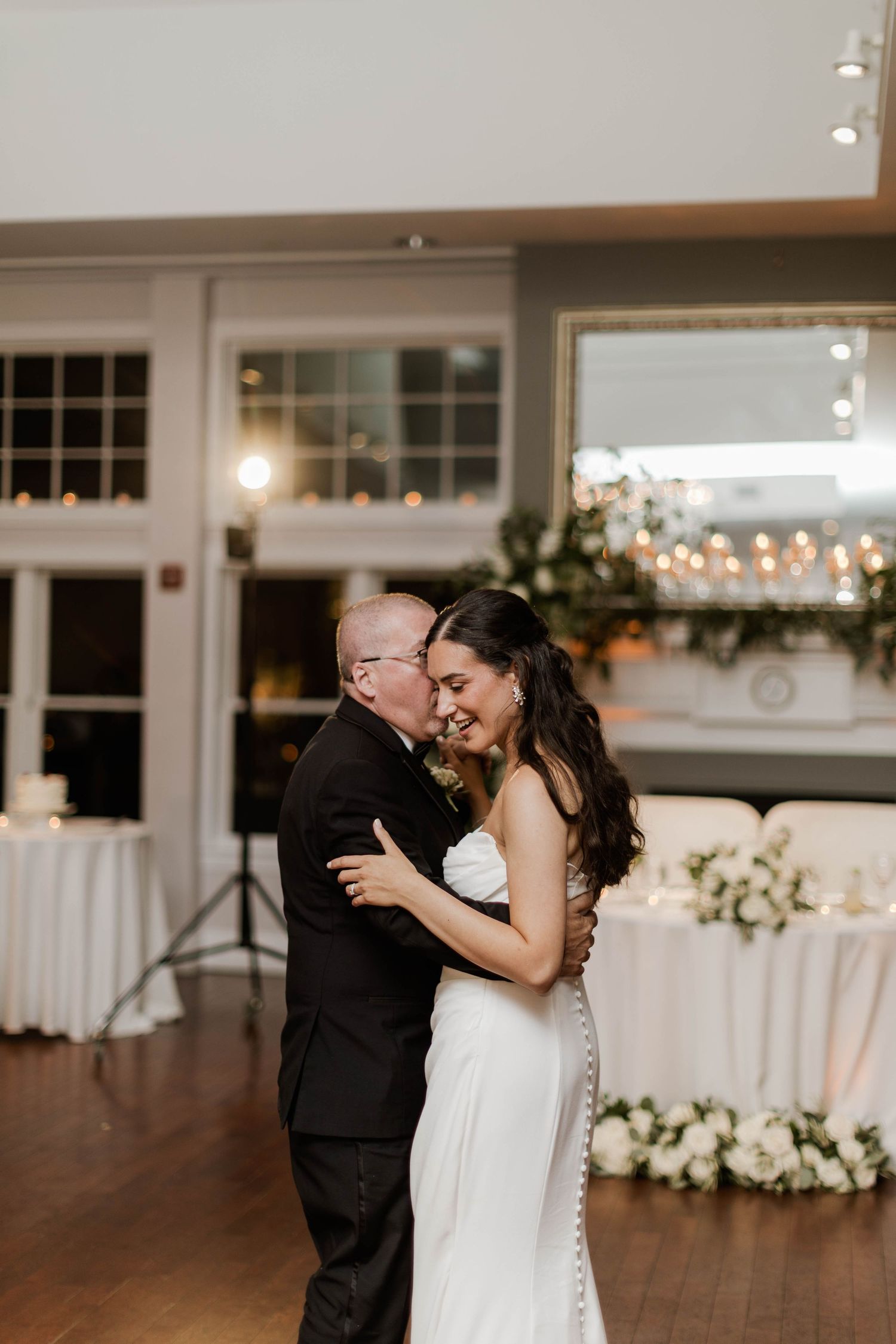Bride shares emotional father-daughter dance at wedding reception with white floral decor.