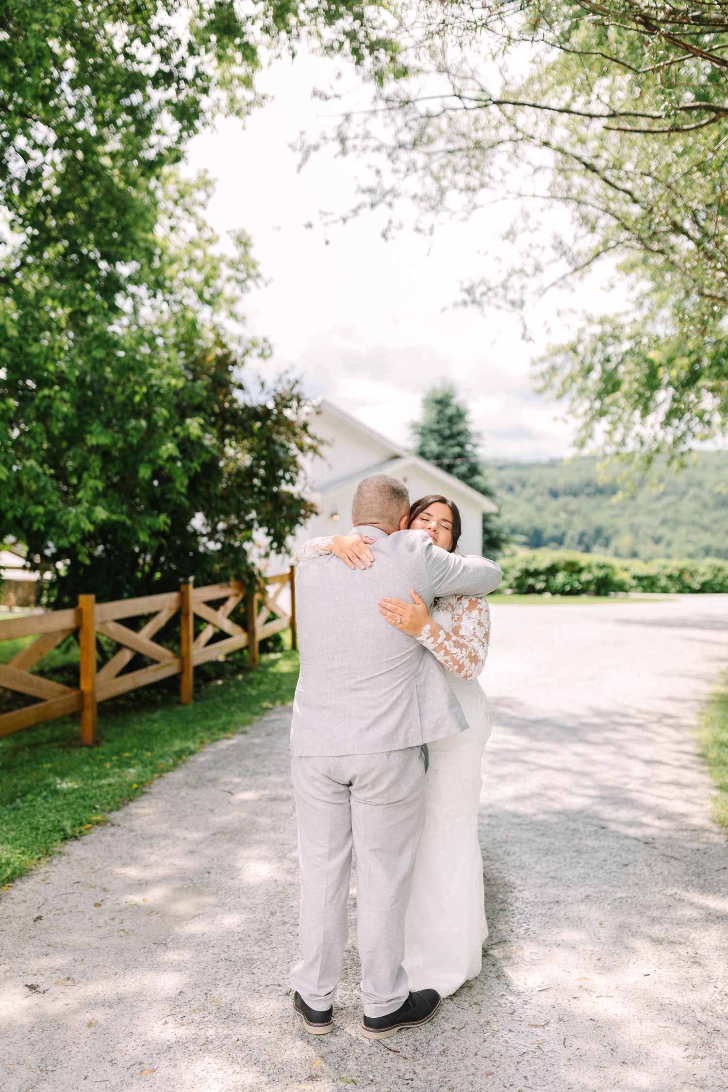 Bride and groom share a heartfelt embrace during their outdoor wedding first look near a wooden fence.