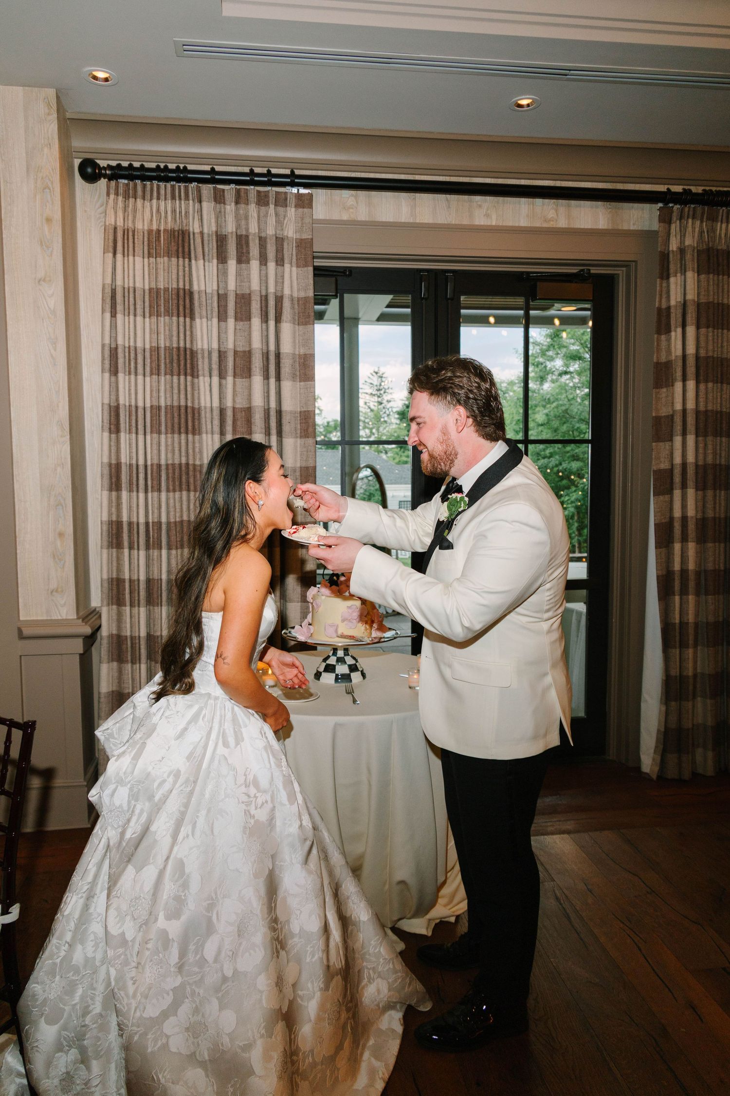 Bride and groom in elegant attire share cake cutting moment at wedding reception.