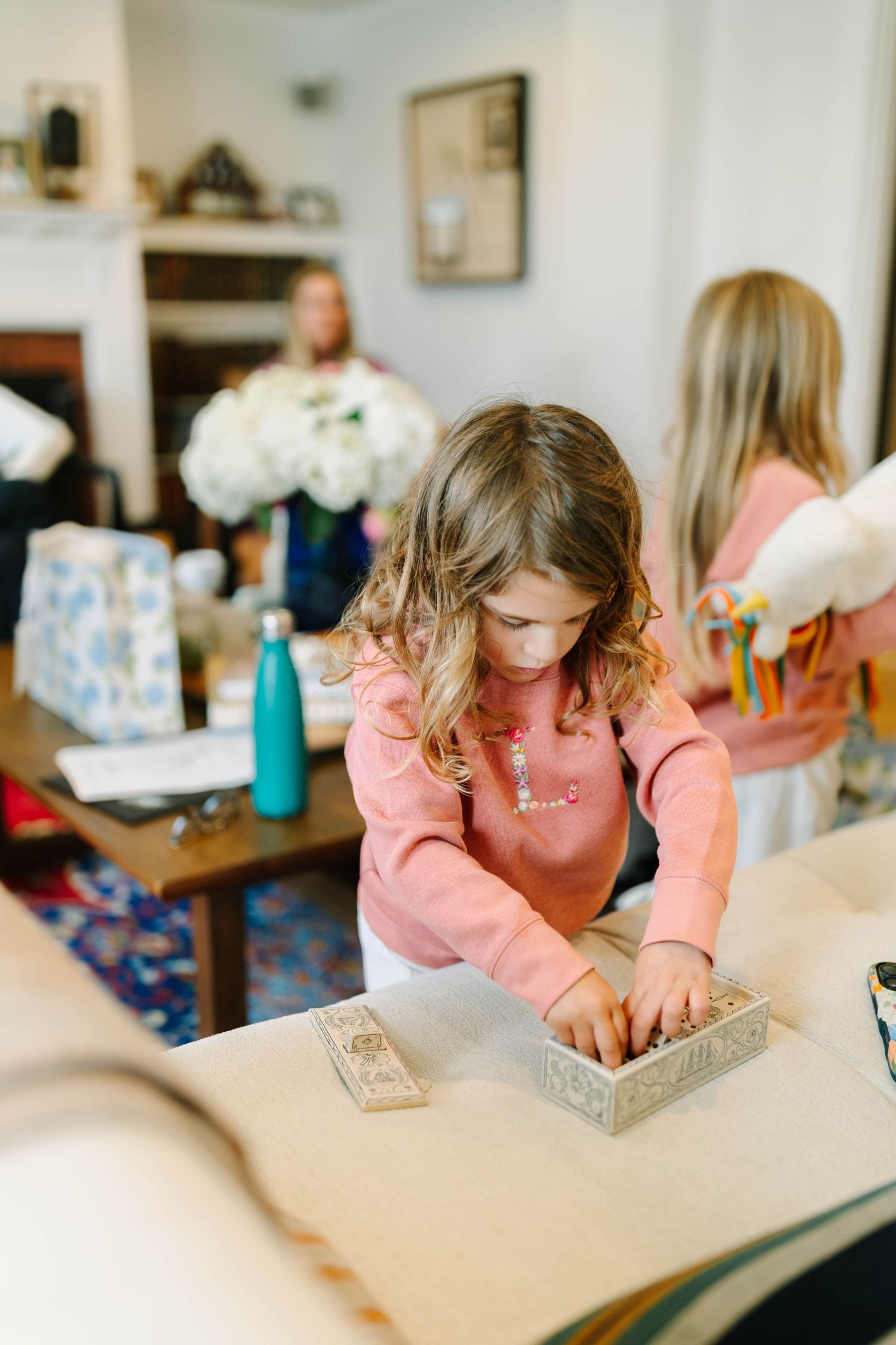 Young girl in pink sweater carefully arranges items on a table during a wedding celebration at home.