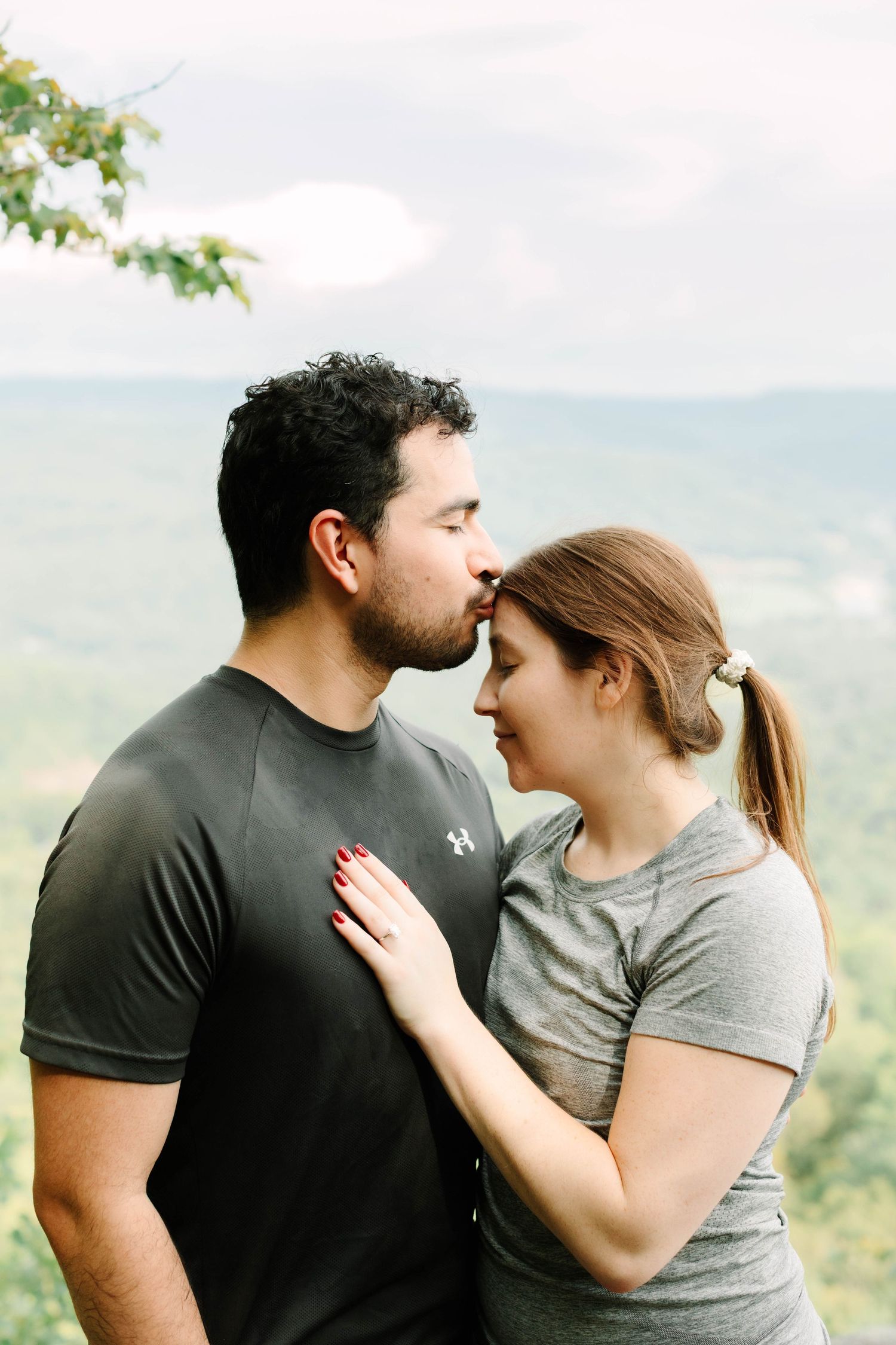 Romantic couple sharing a kiss on a scenic mountain overlook surrounded by green trees.