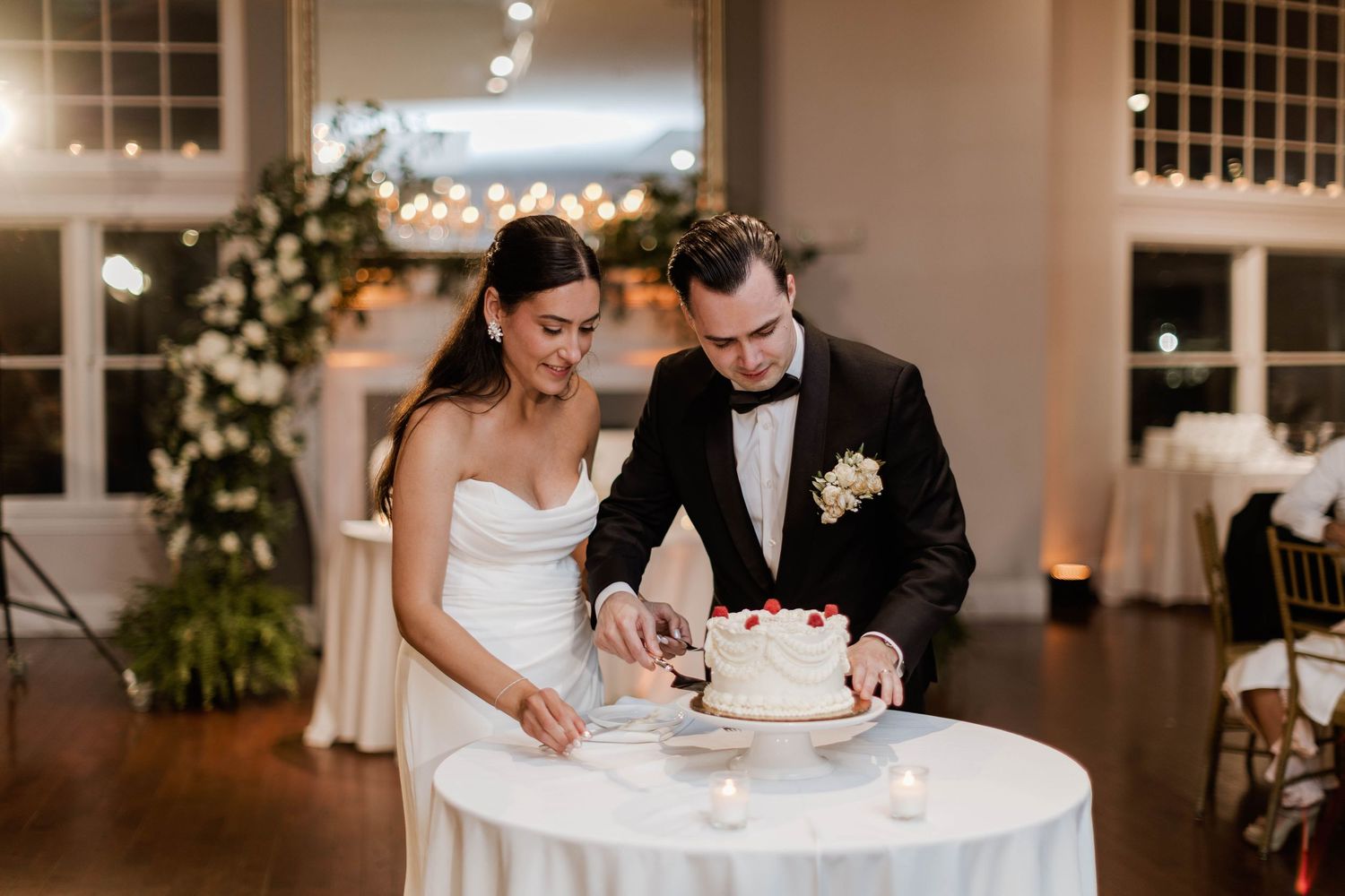 Bride and groom cutting white wedding cake together at candlelit reception table.