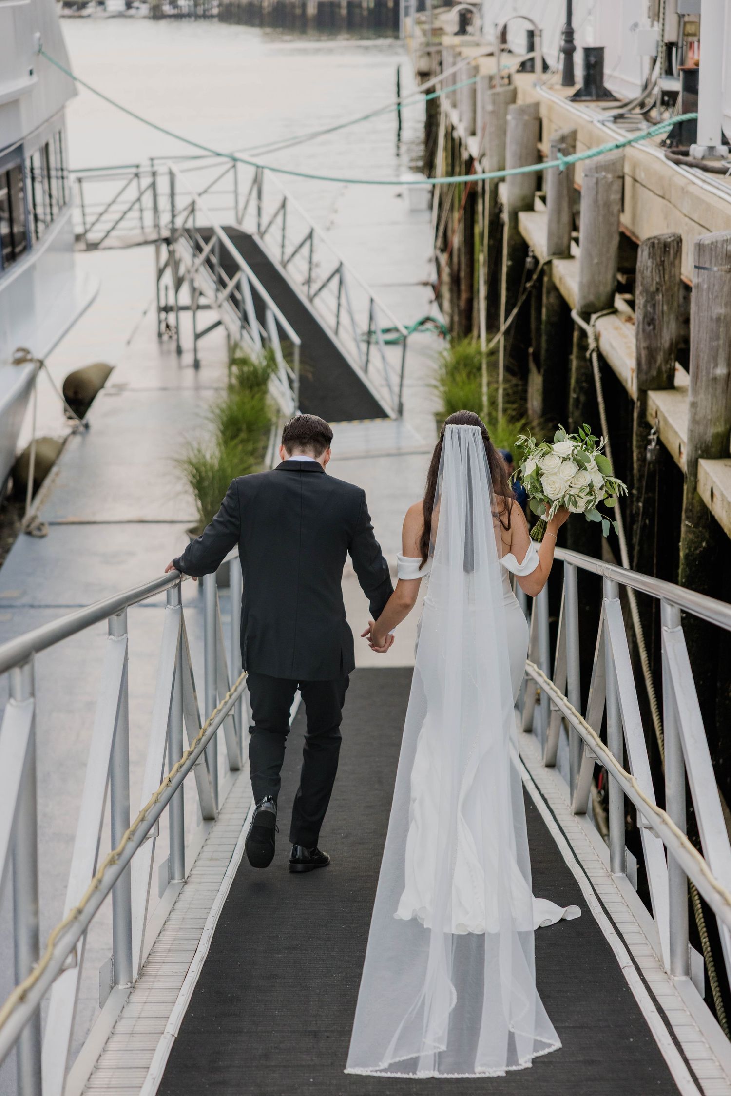Bride and groom walking hand in hand along marina dock after wedding ceremony.