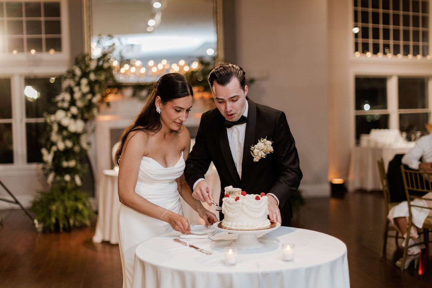 Bride and groom cutting elegant white wedding cake with strawberries at candlelit reception.