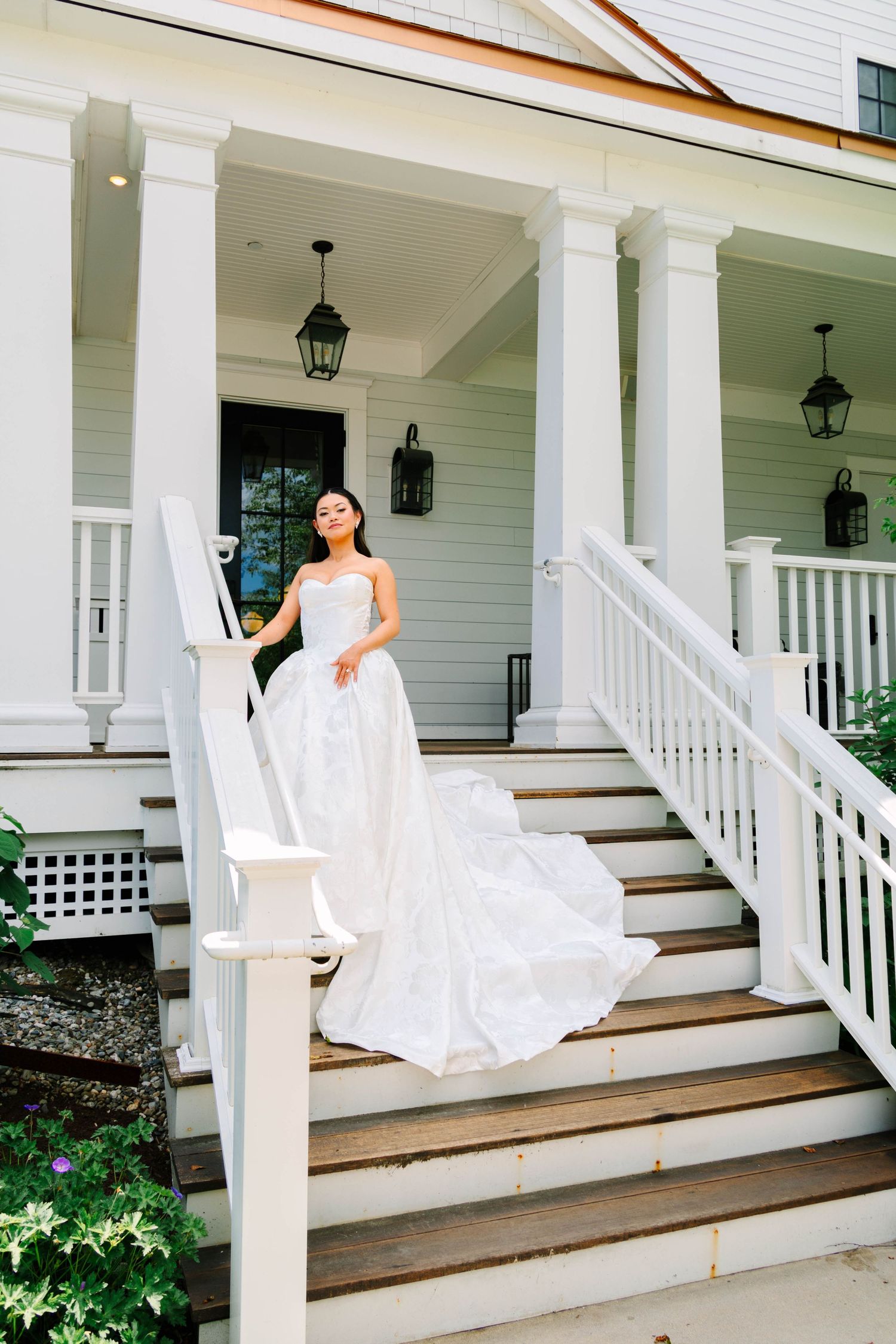 Bride in white floral ballgown posing on steps of elegant white colonial venue.