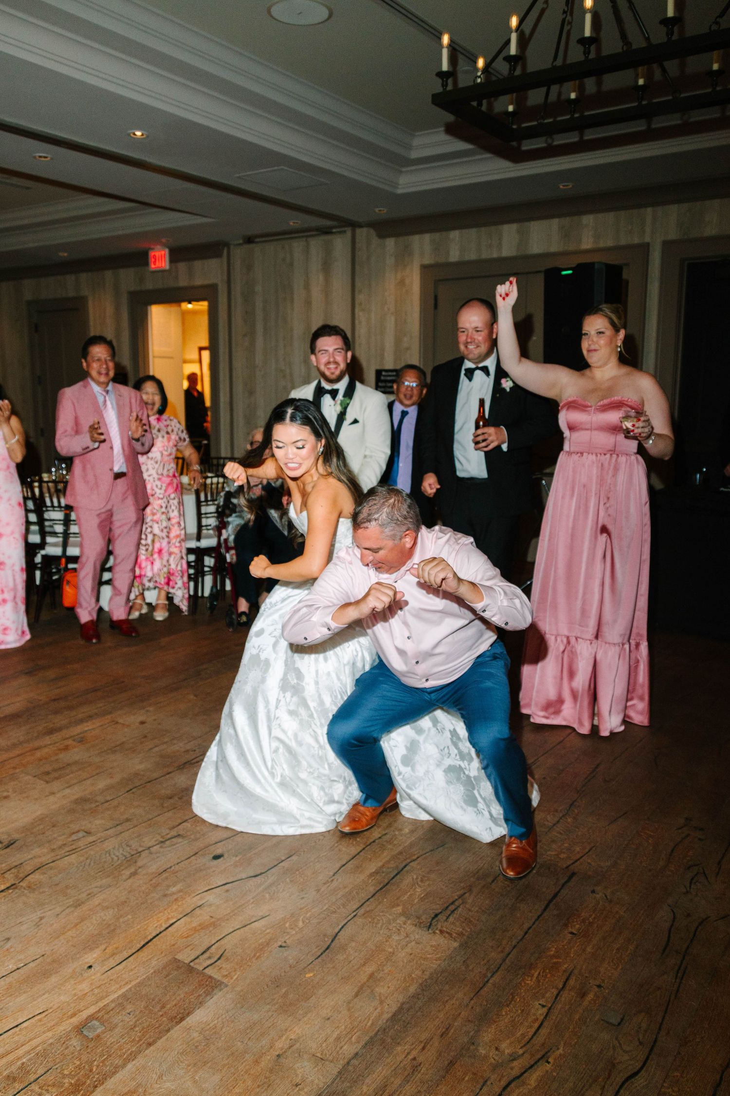 Bride and guest dancing energetically on the wedding reception dance floor while guests cheer.