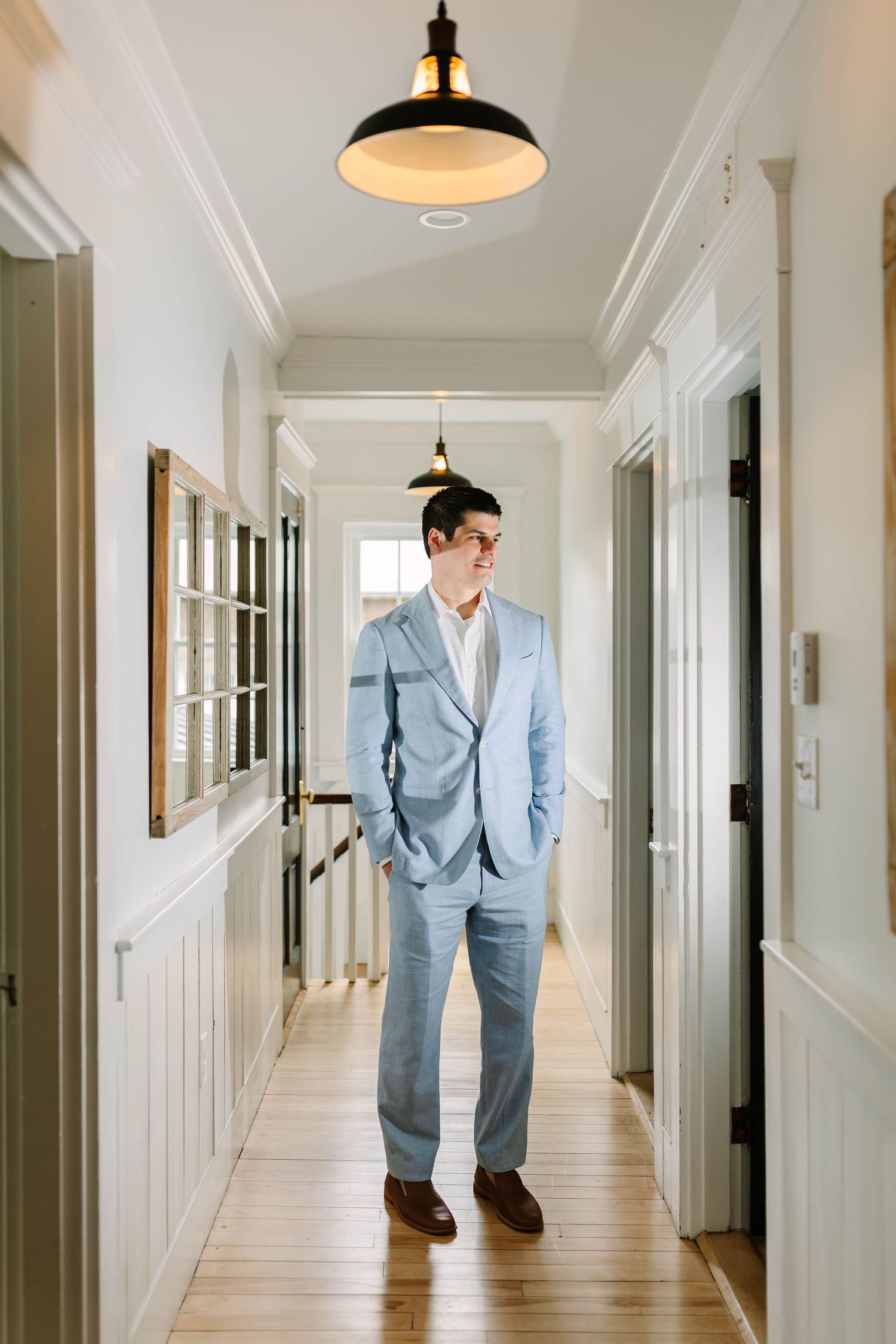 Groom in light blue suit stands confidently in hallway before wedding ceremony.