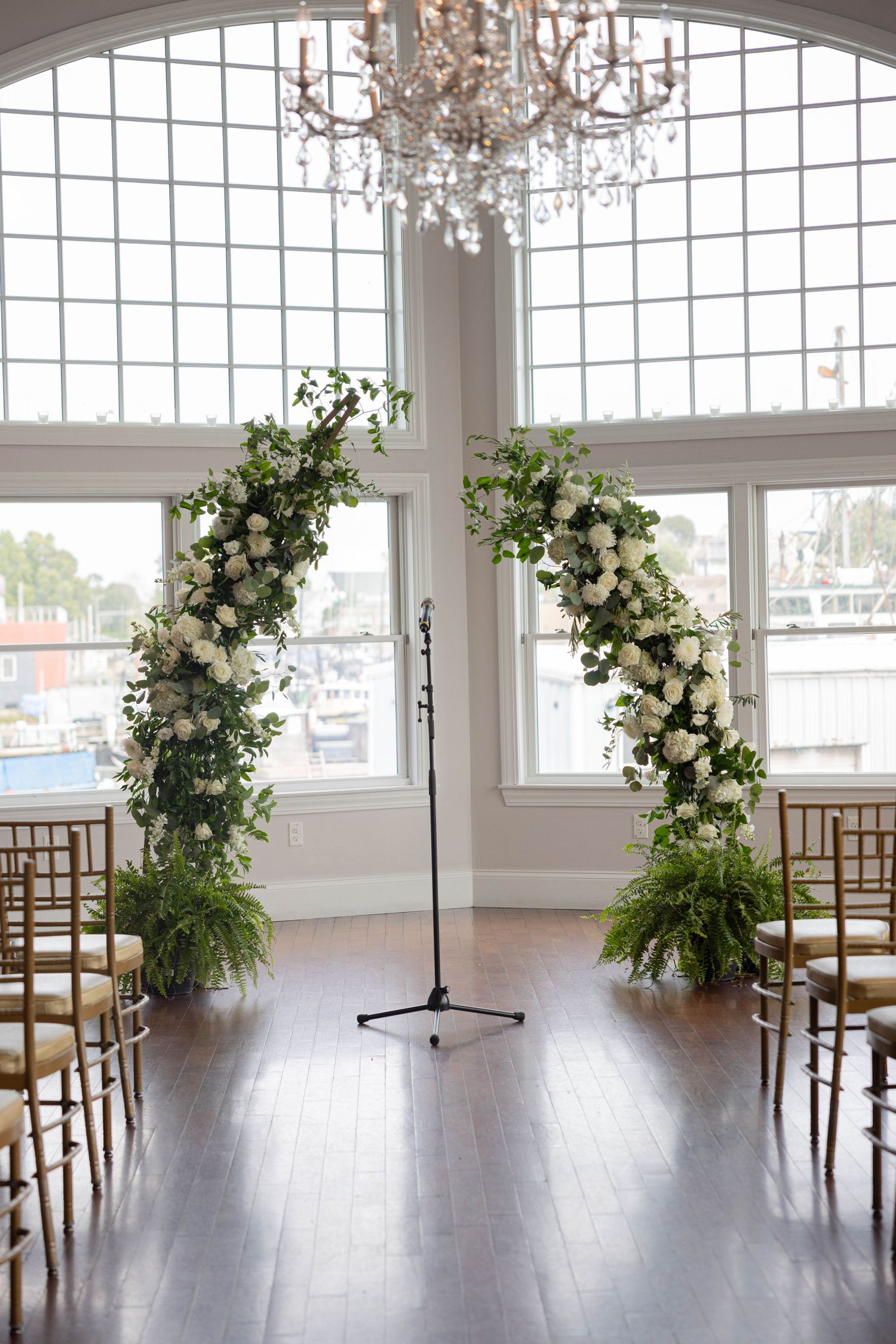 Elegant indoor wedding ceremony arch with white roses and greenery under a crystal chandelier.
