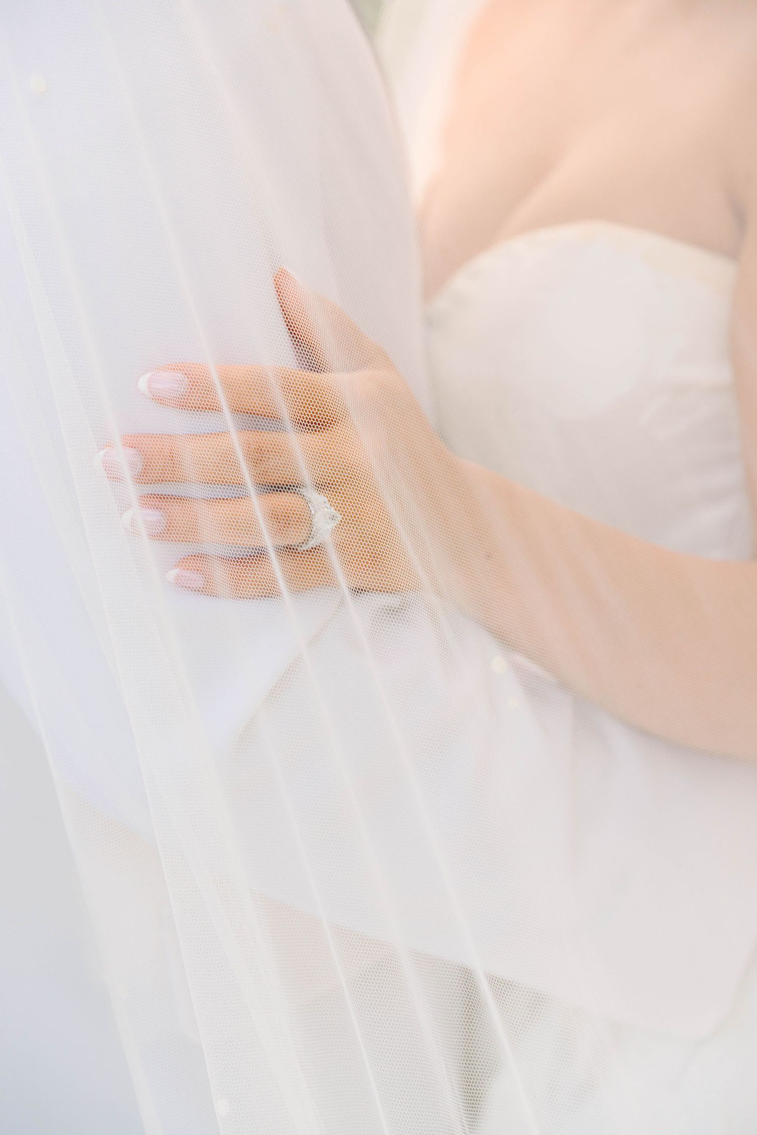 Close-up of bride's hand holding white wedding veil, showcasing elegant diamond engagement ring and manicured nails.